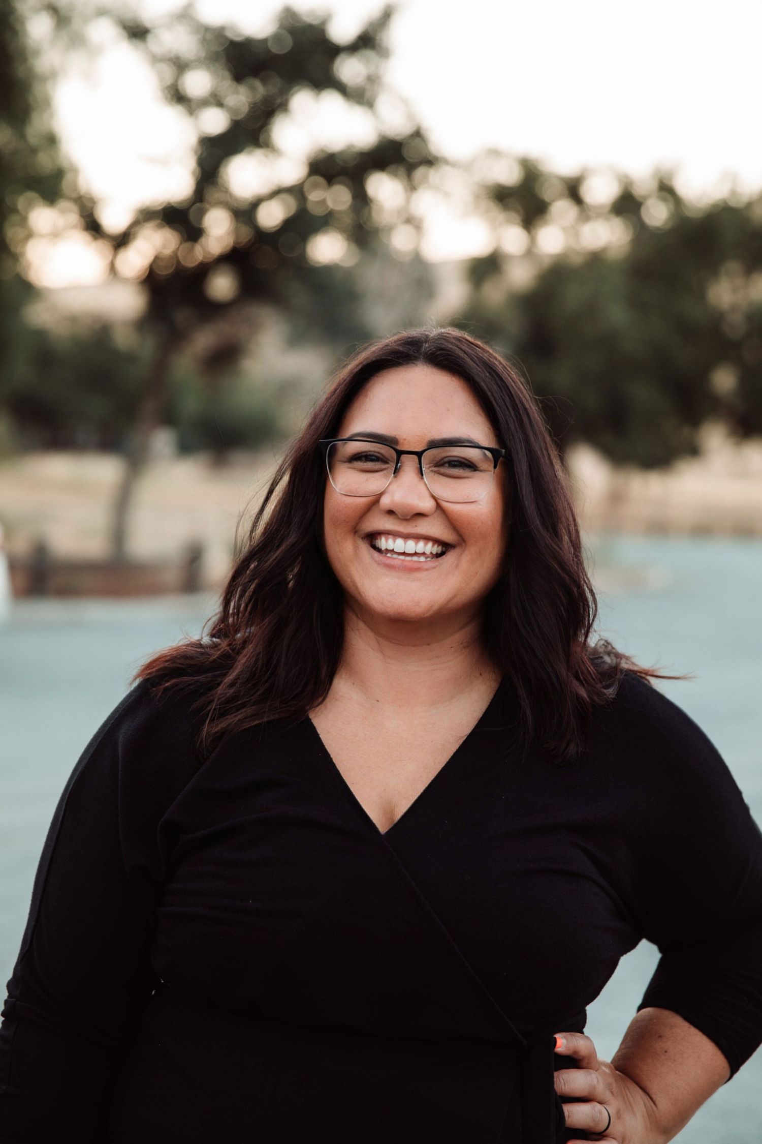 Professional headshot of photographer in black top against blurred outdoor background.