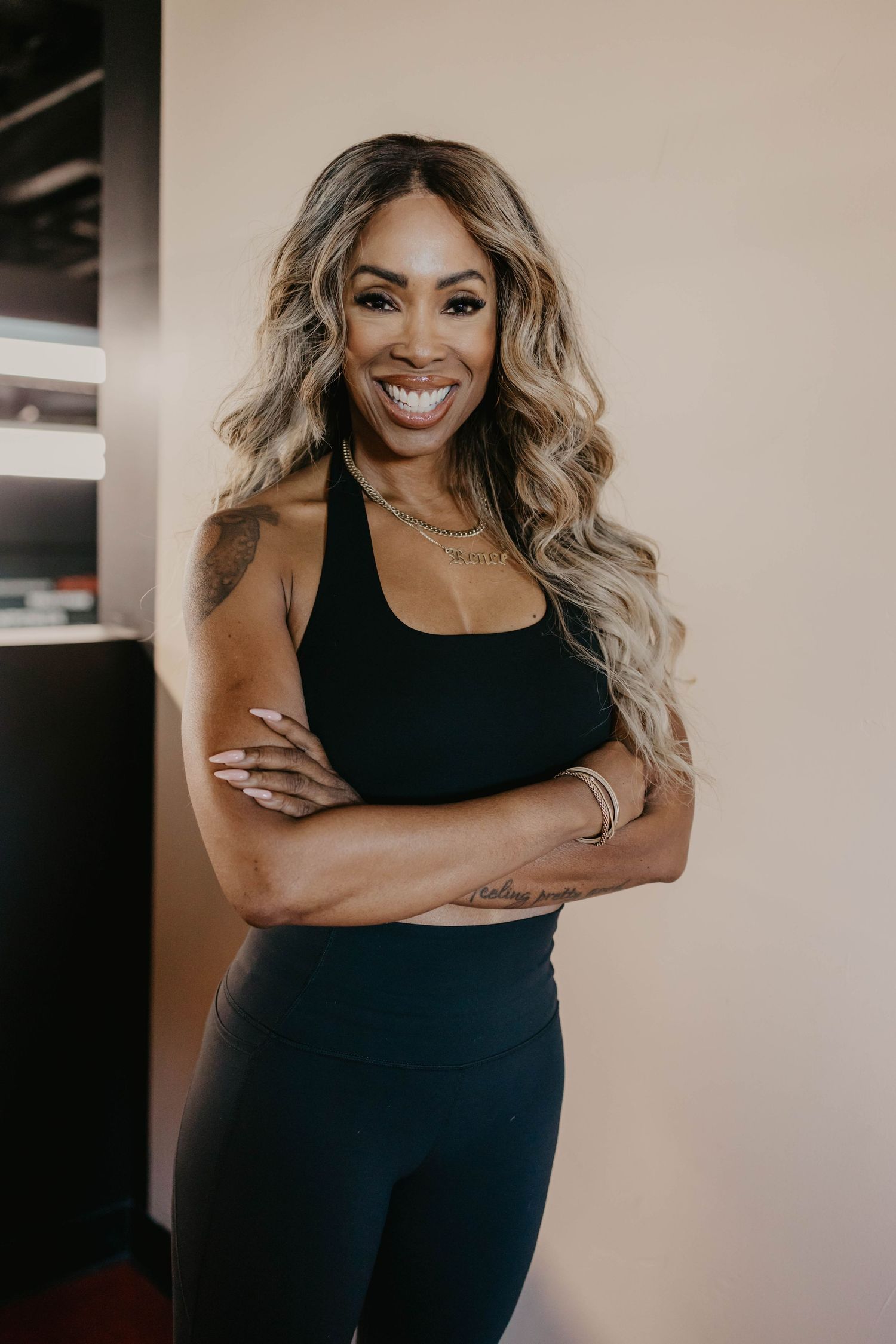Fitness instructor in black athletic wear poses against beige wall.