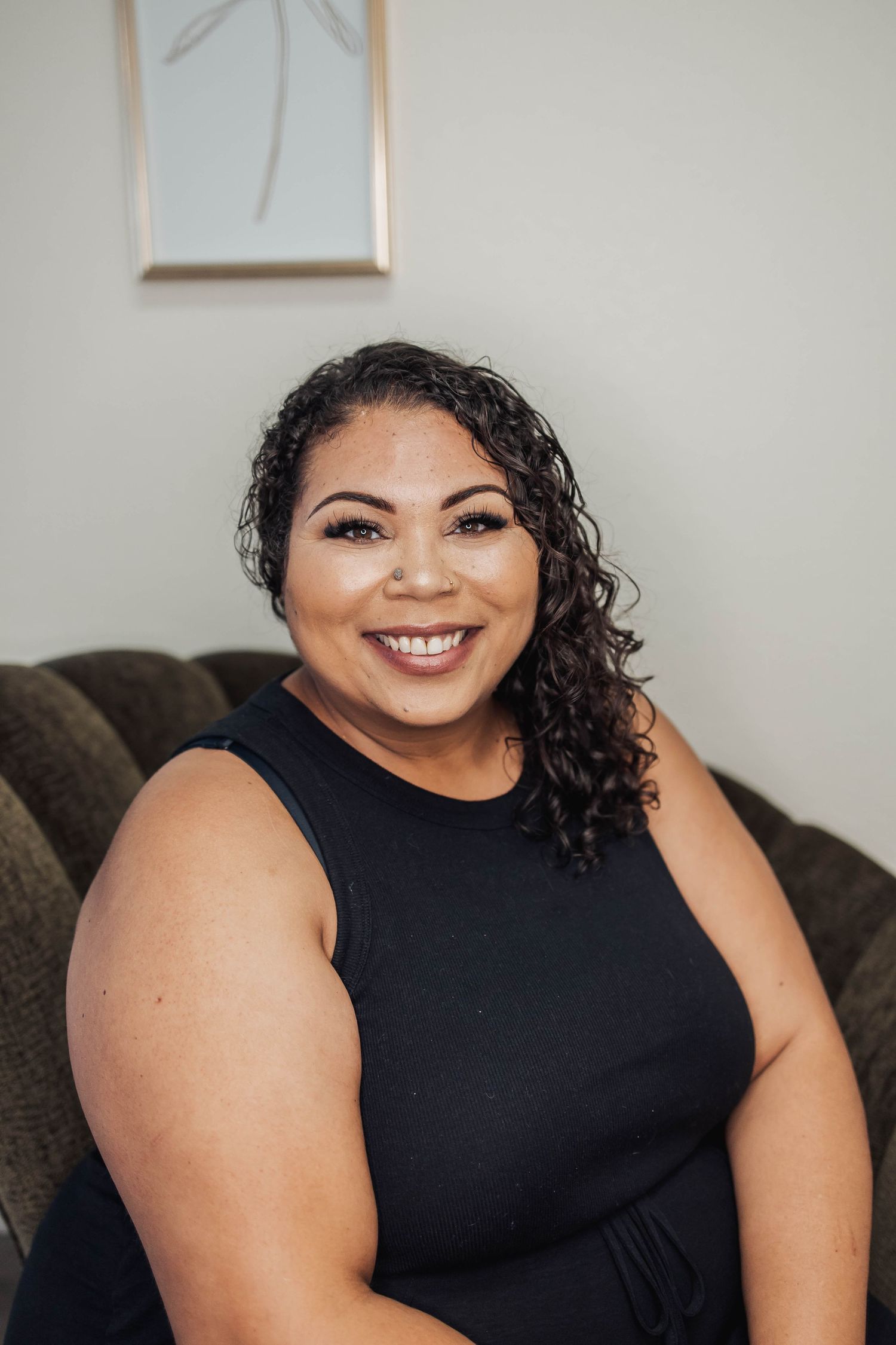 Person in black sleeveless top smiling against neutral background.