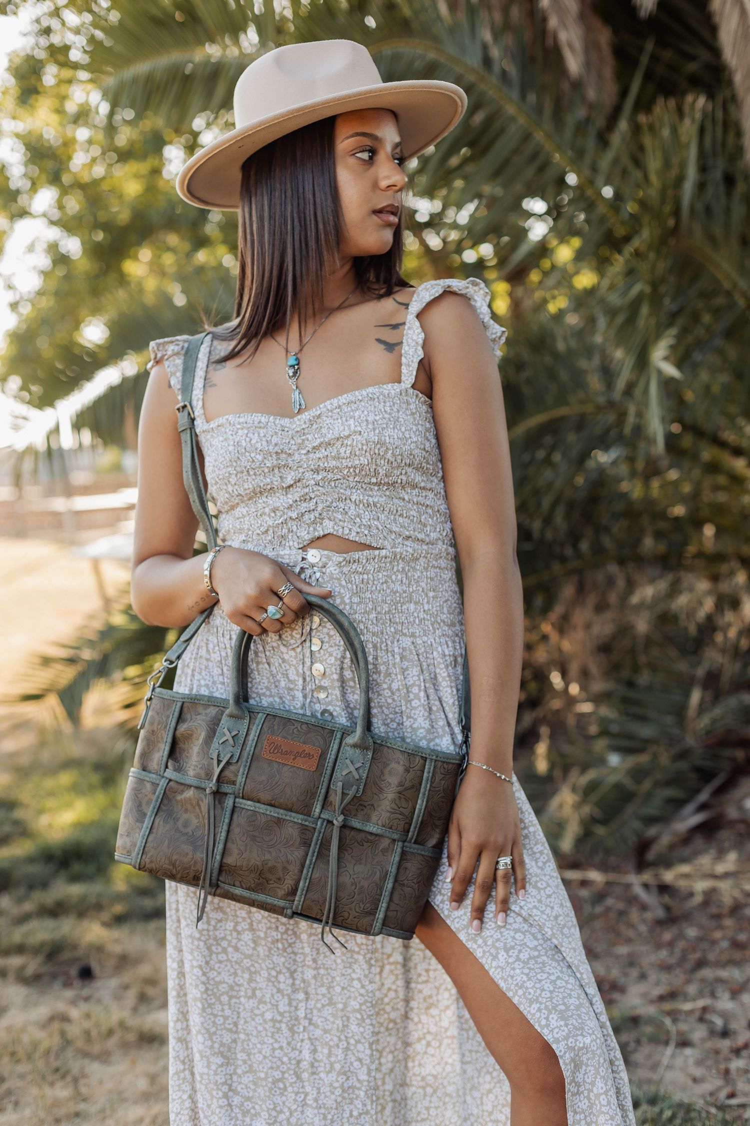 Brown leather satchel bag styled with white summer dress and wide-brim hat outdoors.