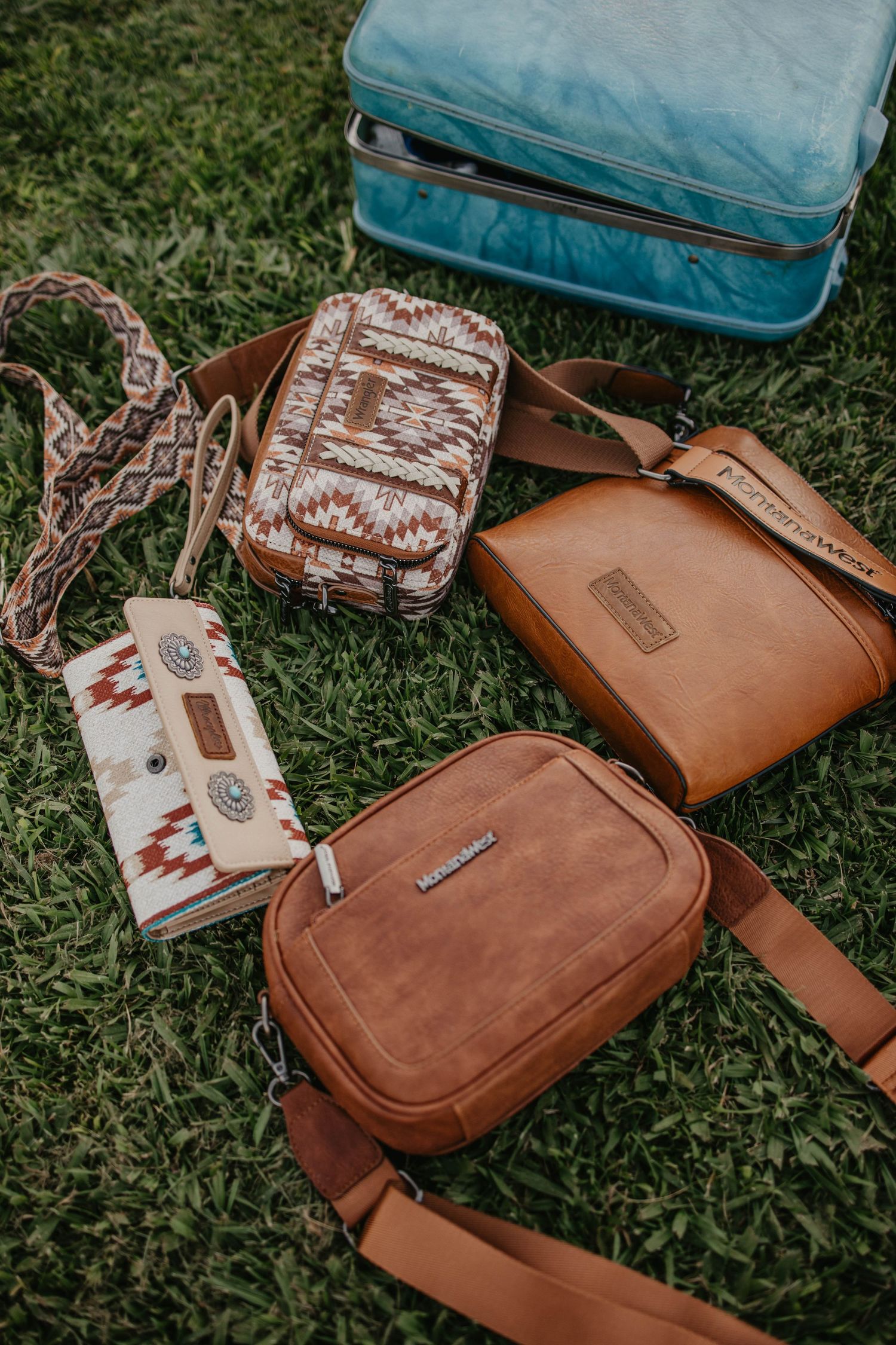 Collection of leather bags and wallets with southwestern patterns laid on grass.