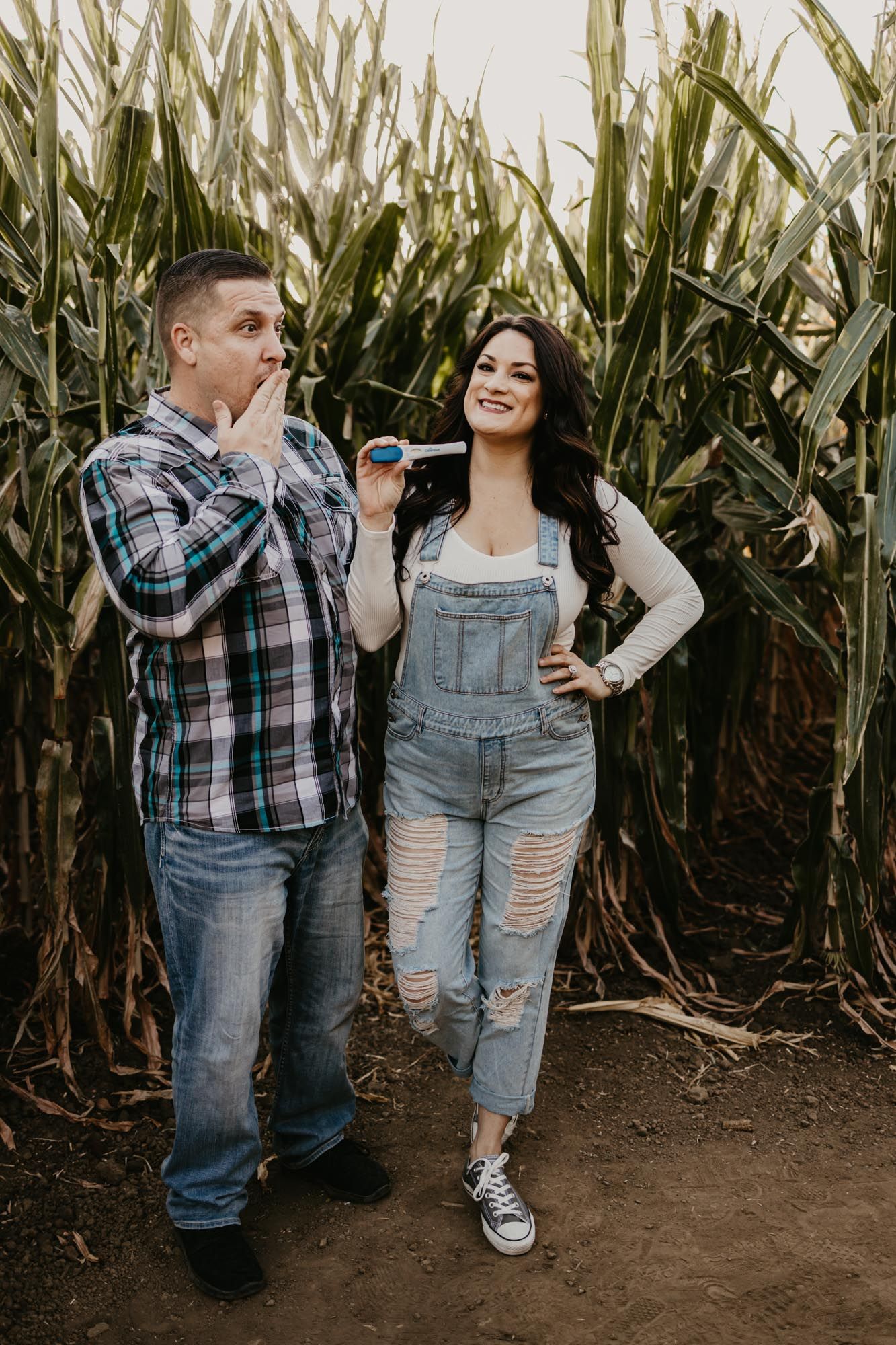 Couple playfully blowing party horns during pregnancy reveal photoshoot in corn maze.