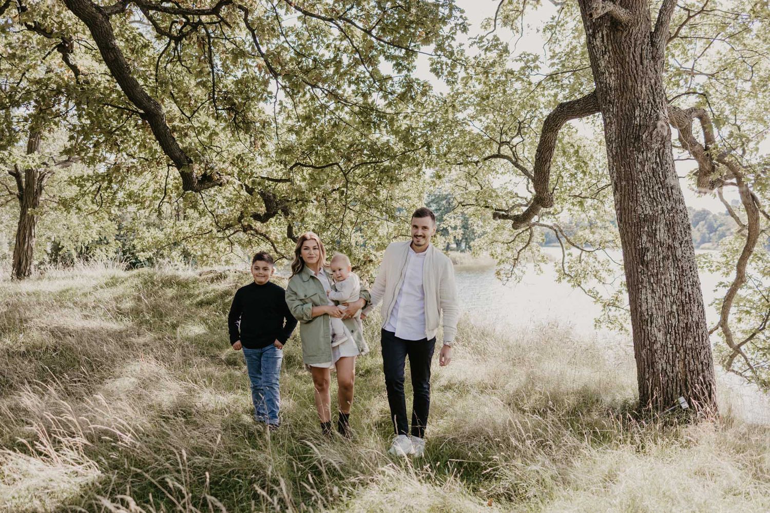 Family walking together through sunlit oak grove on grassy hillside.