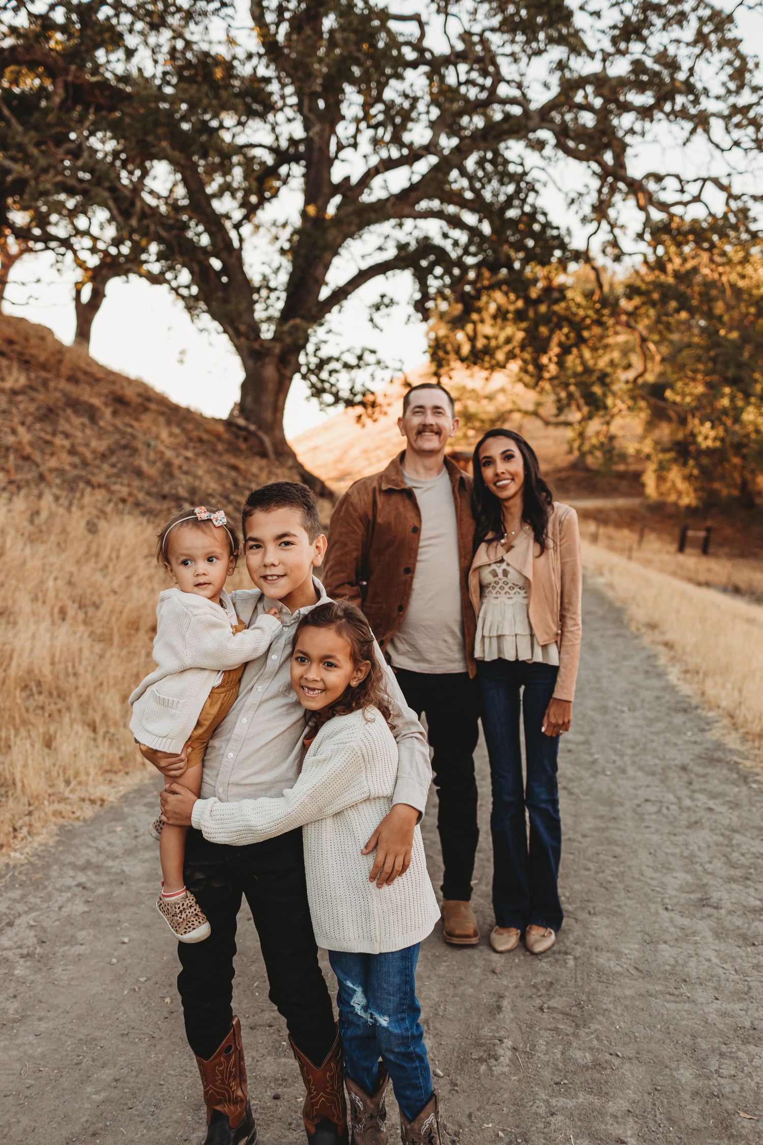 Portrait of family members posing together on a hiking trail at sunset with rolling hills behind them.