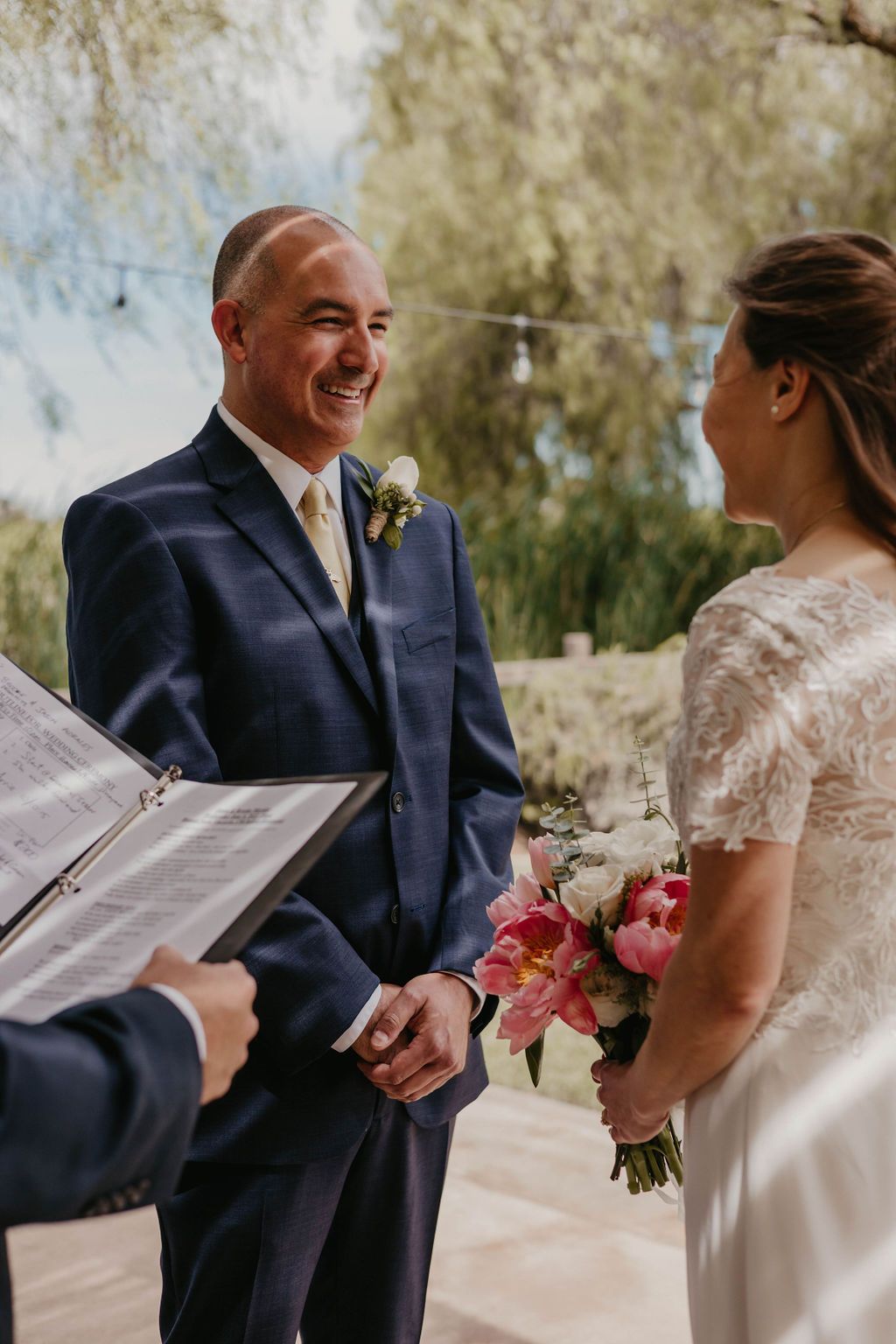 A joyful moment during a wedding ceremony on an outdoor patio with pink floral bouquet.
