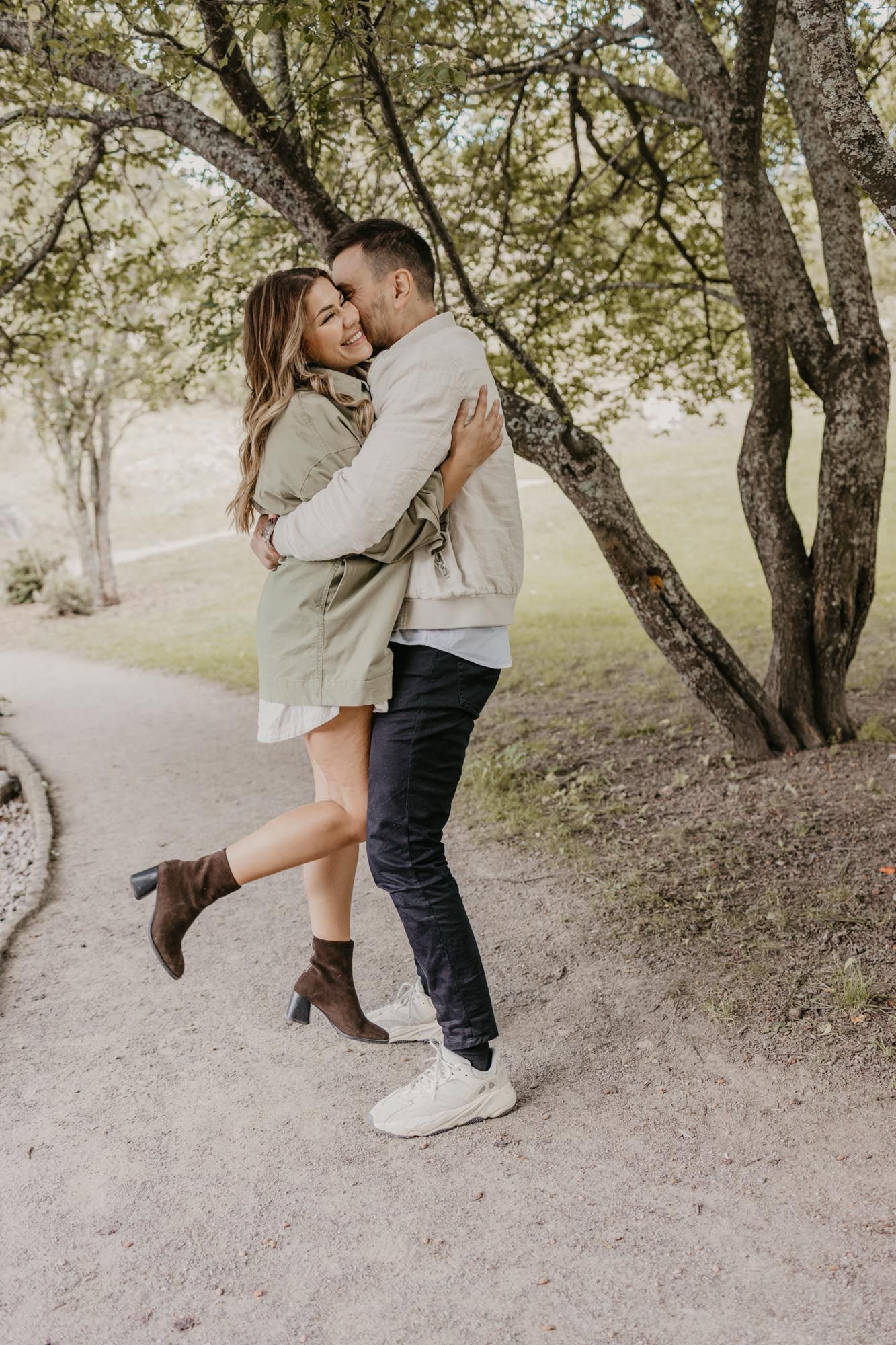 A couple poses playfully on a nature trail with trees in the background.