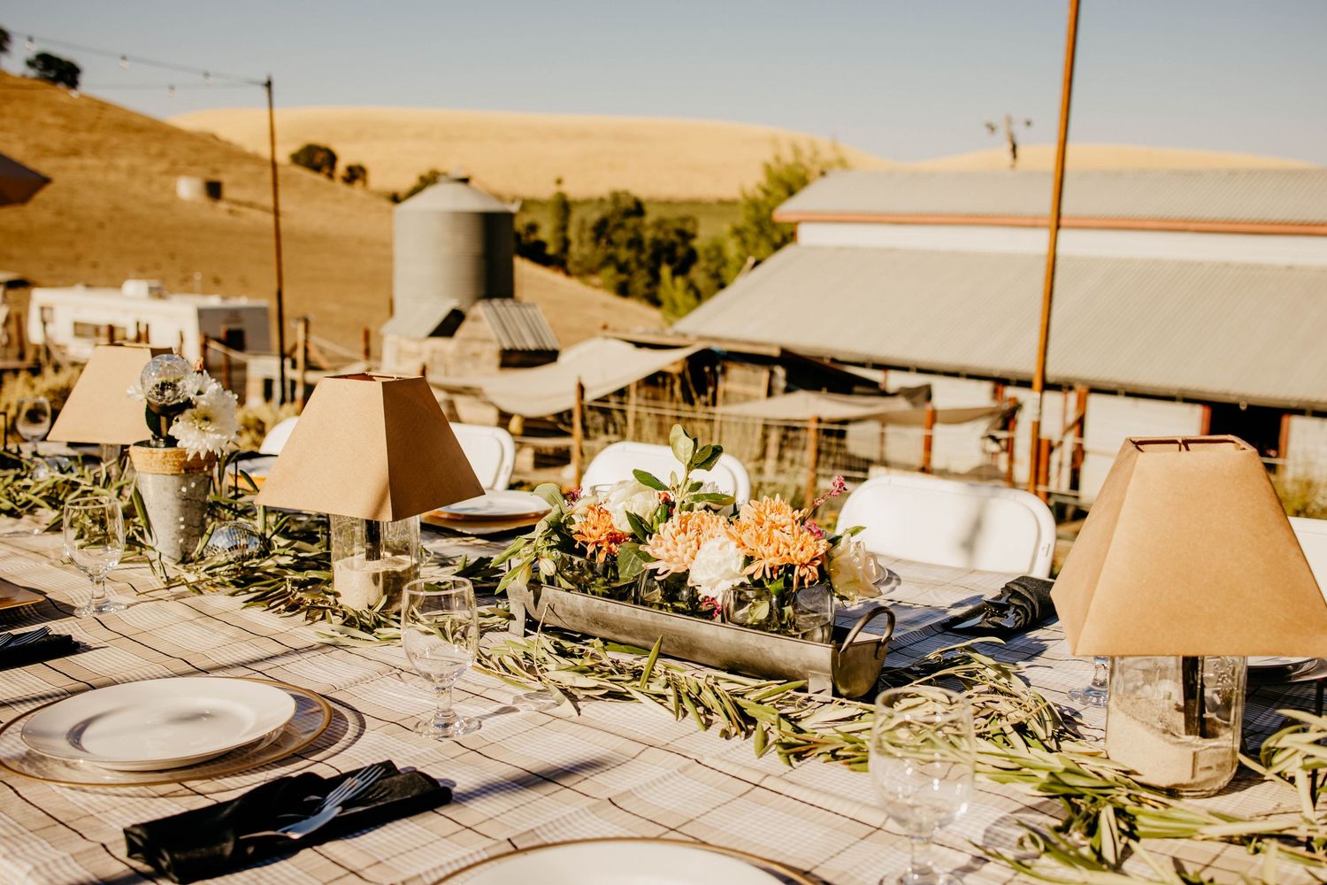 Outdoor event setup with string lights and table settings at sunset.