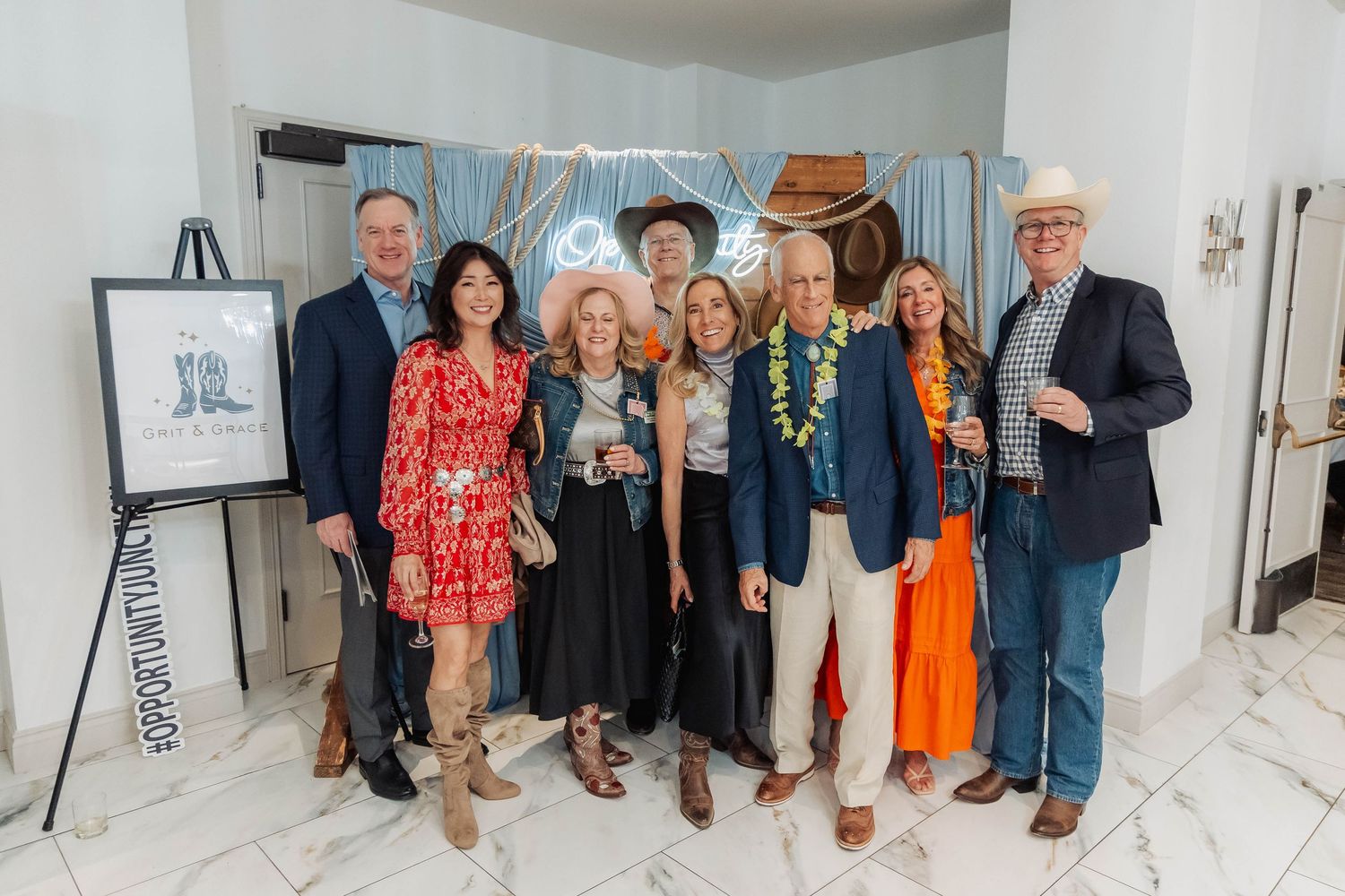 Group of eight adults posing together at a western-themed charity event, dressed in cowboy hats and colorful attire.