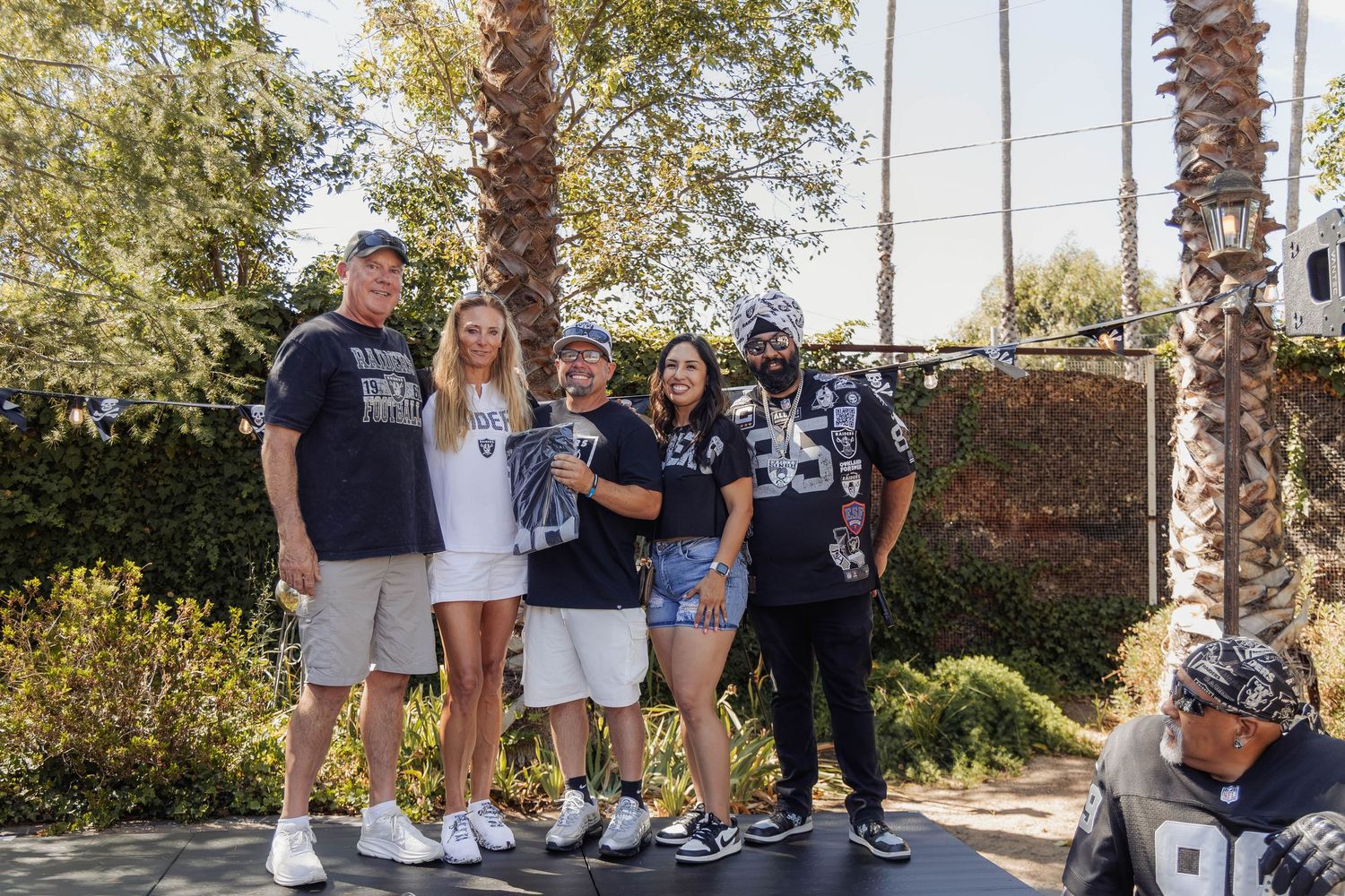 Group of Raiders fans posing together outdoors near palm trees on a sunny day.
