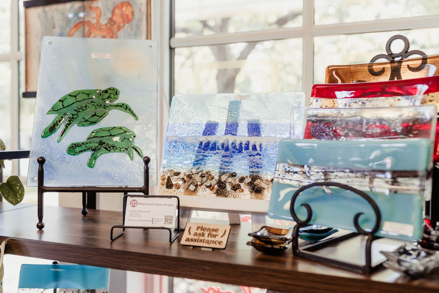 Display of coastal-themed art and decorative items in a sunny shop window.