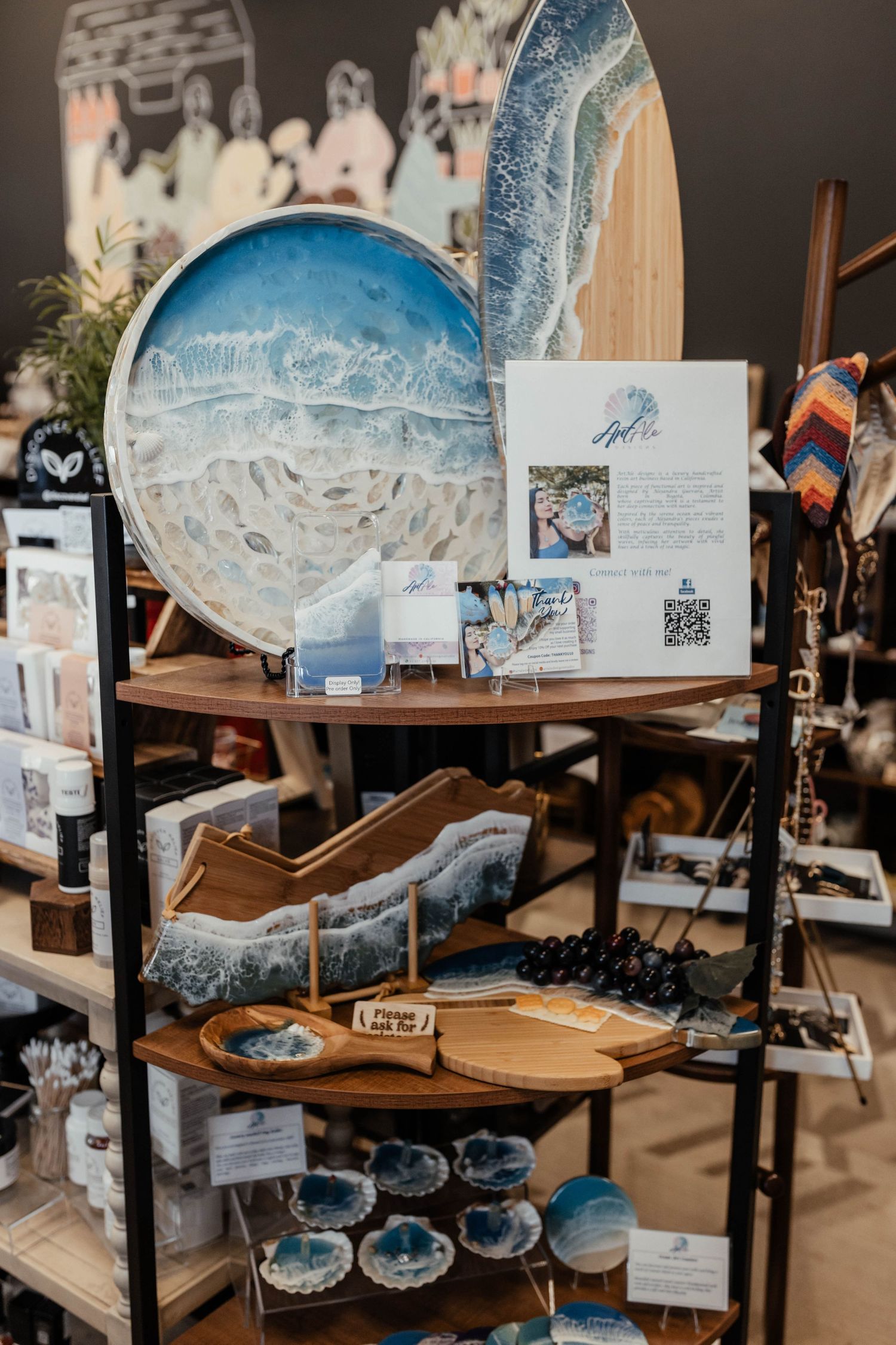 Artisanal gift shop display featuring blue ceramic plates, decorative items and framed artwork on wooden shelves.