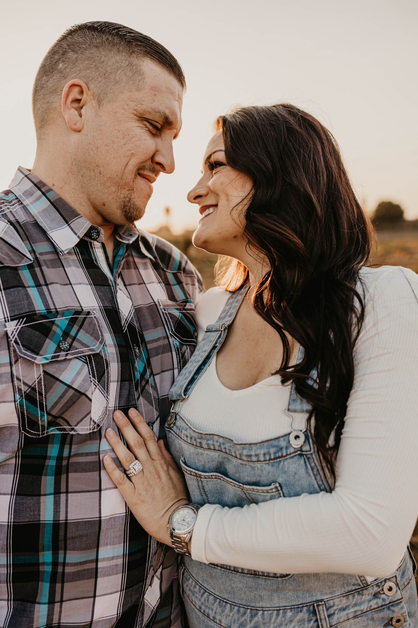 A couple laughs together during their engagement photos, with soft golden light in the background.