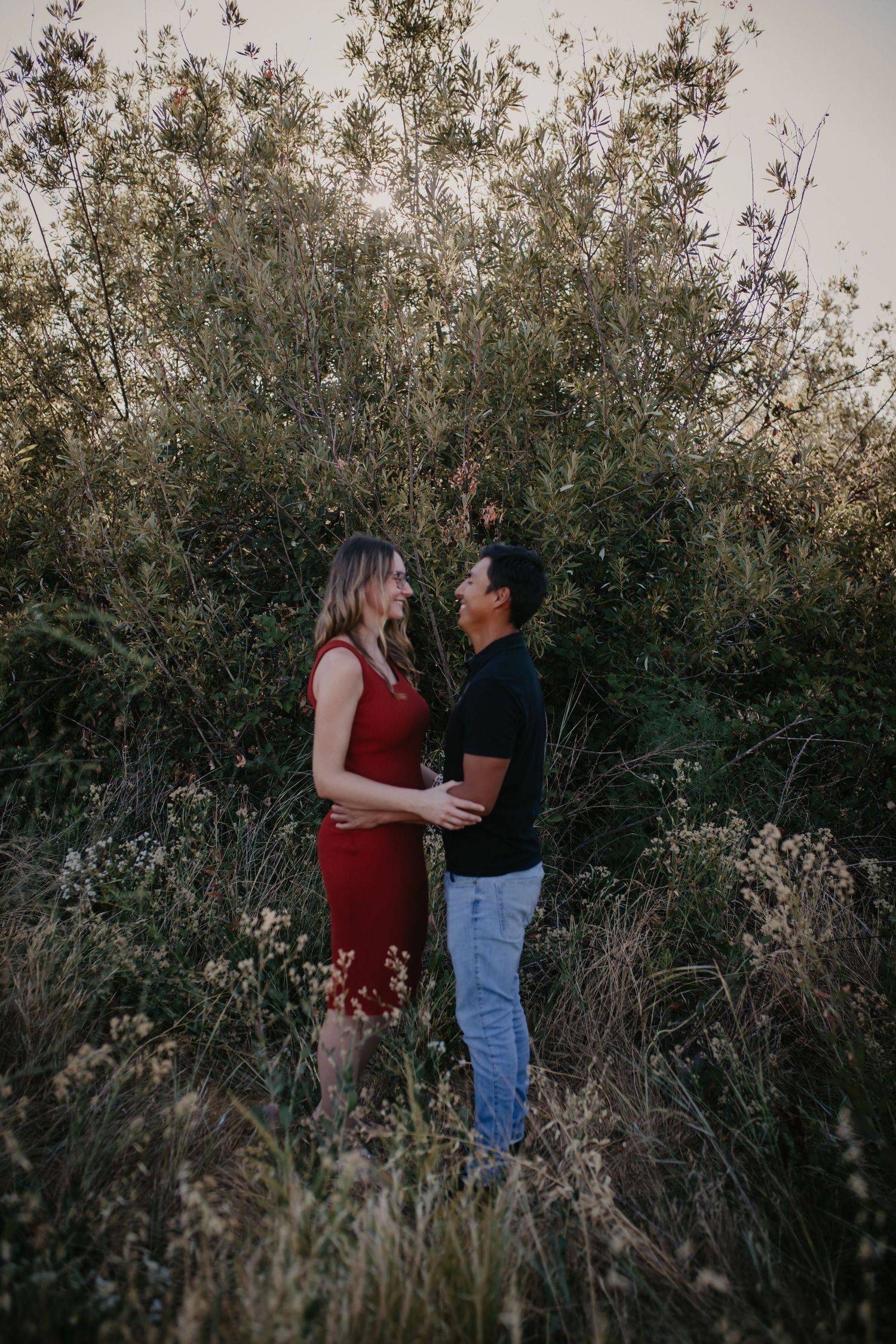 A couple stands together among wild grasses during a moody sunset photoshoot.