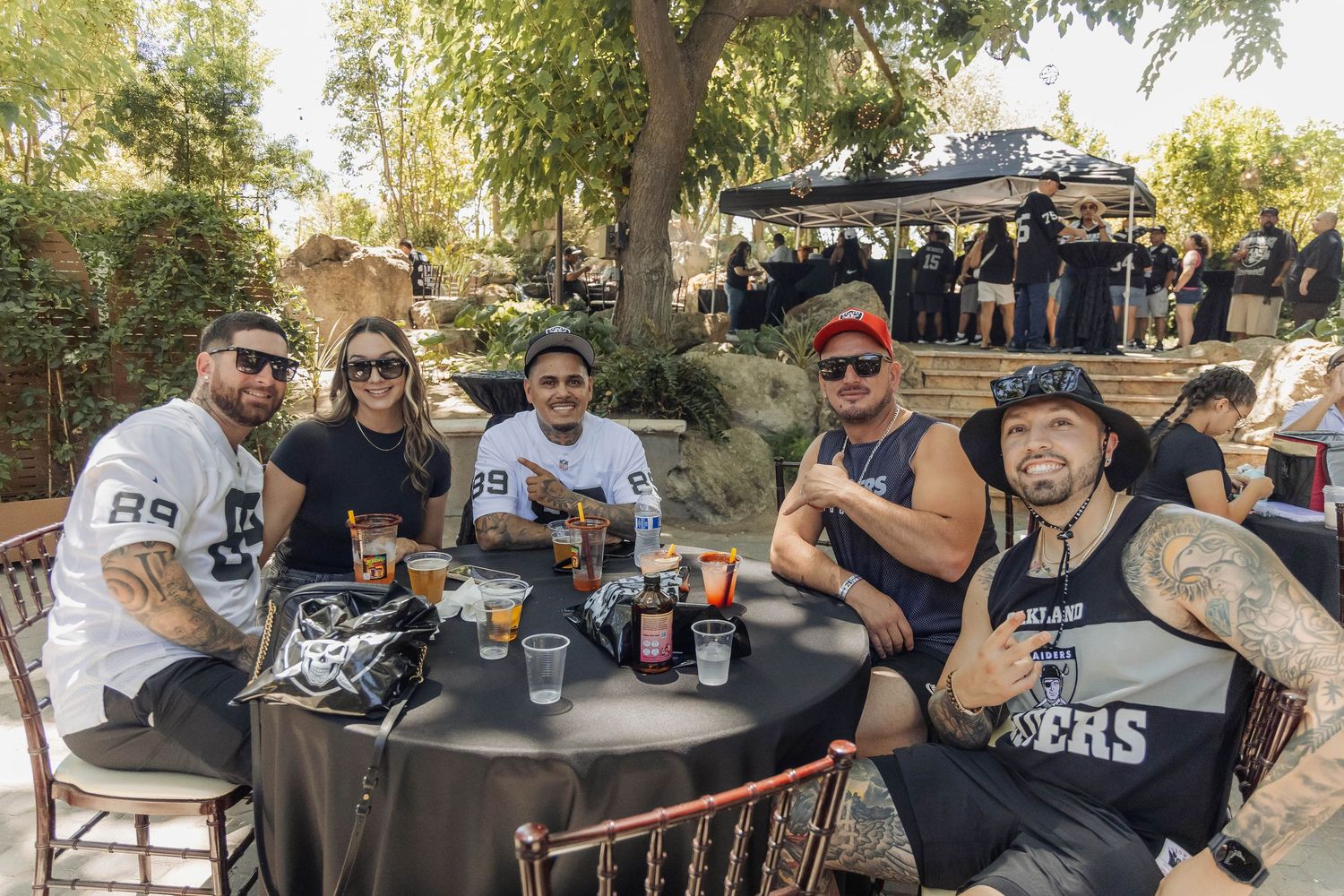 Group of Raiders fans smiling at a table during an outdoor tailgate party event.