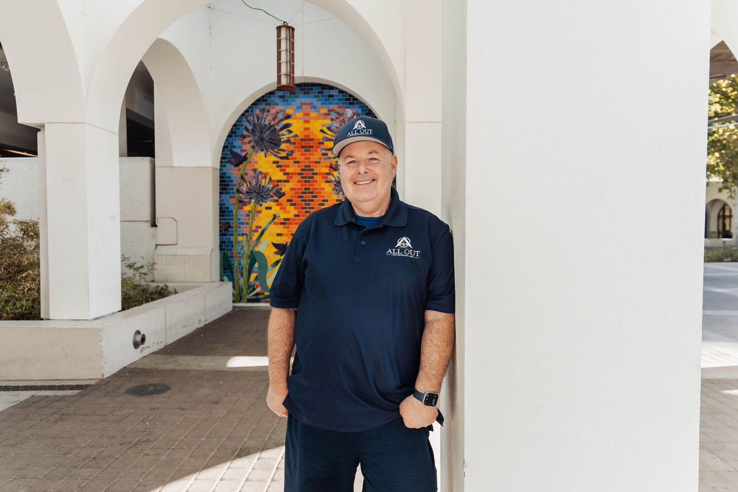 A person in a navy blue t-shirt stands in front of white arched architectural columns.