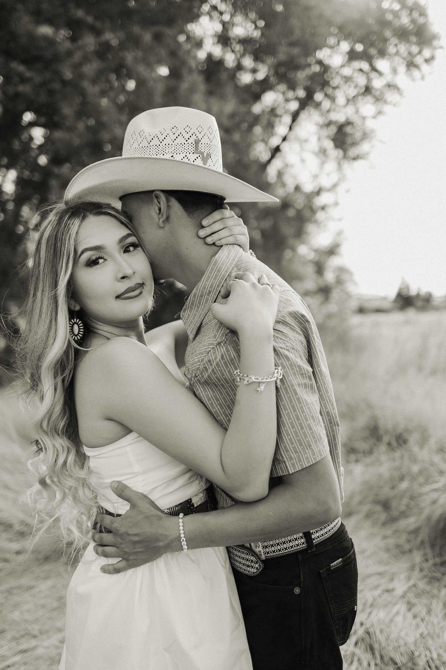 Couple in western attire embracing in black and white outdoor portrait.