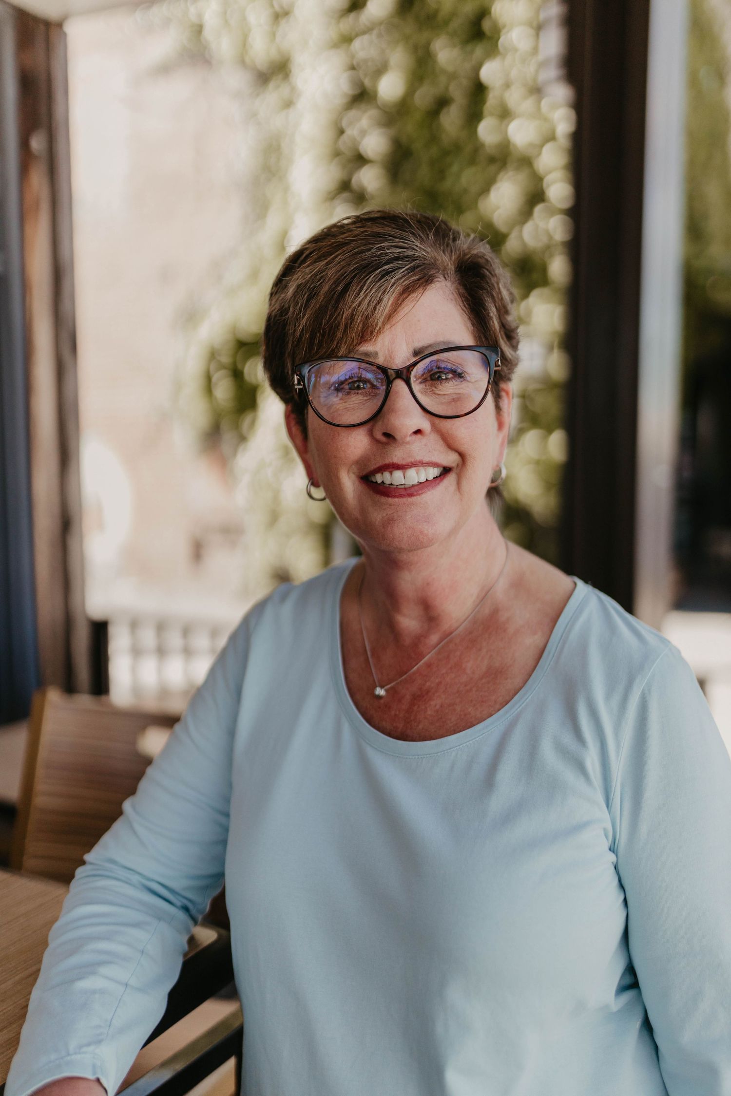 Professional headshots featuring a light blue sweater and cat-eye glasses in a warm outdoor setting.
