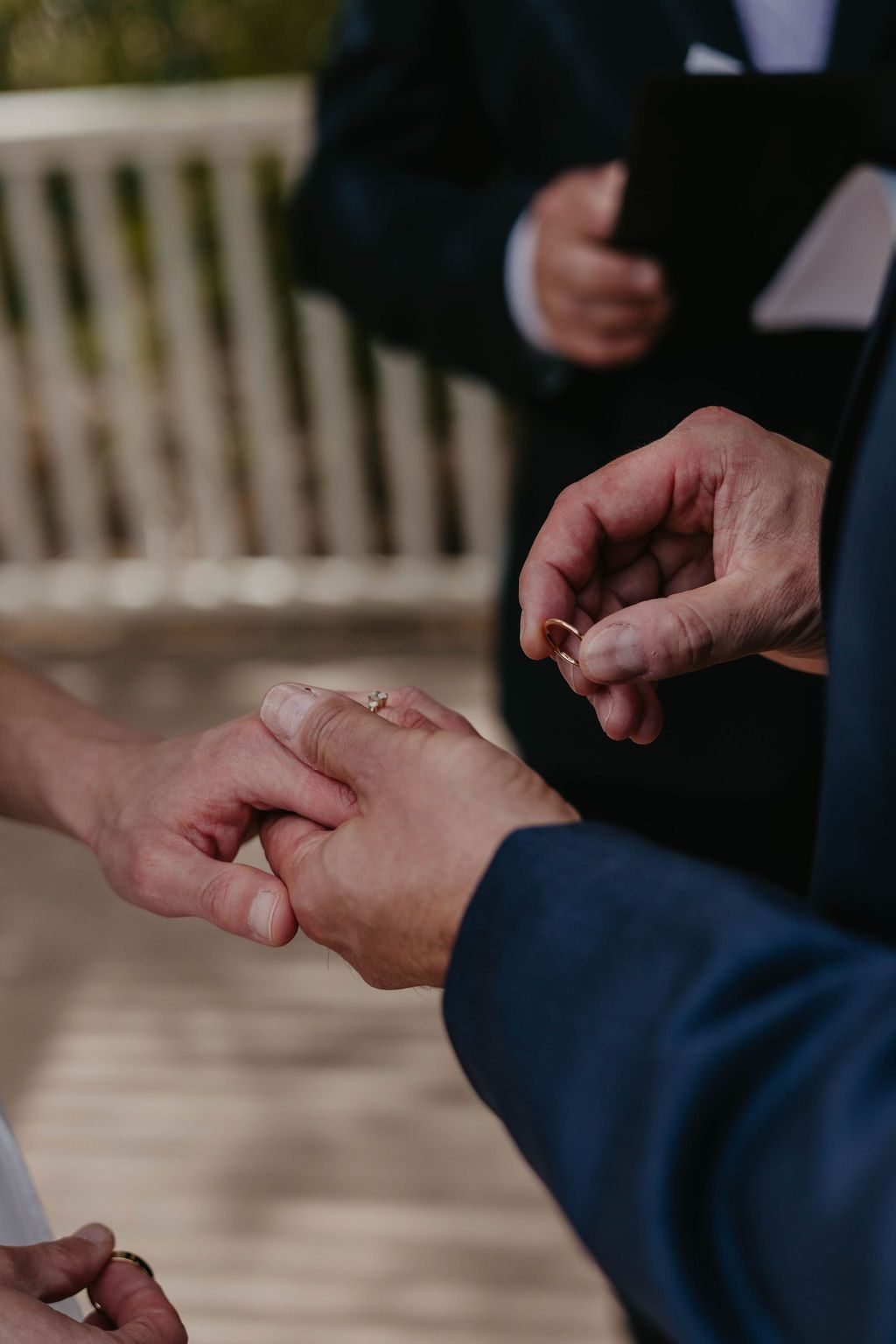 Close-up of hands exchanging wedding rings during an outdoor ceremony.