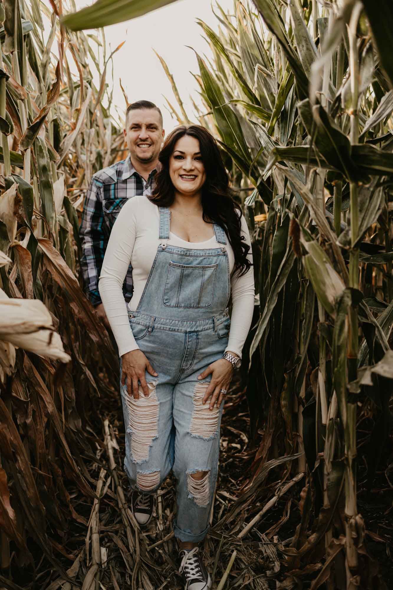 A couple smiles while standing in a corn maze during golden hour.