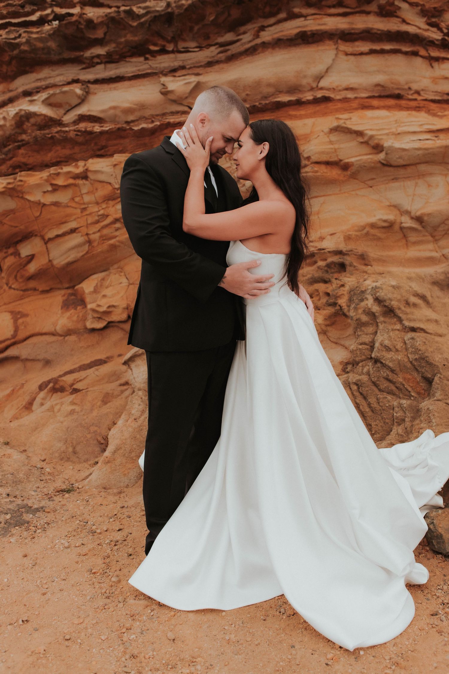 Romantic wedding photo of newlyweds sharing an intimate moment against desert canyon backdrop.