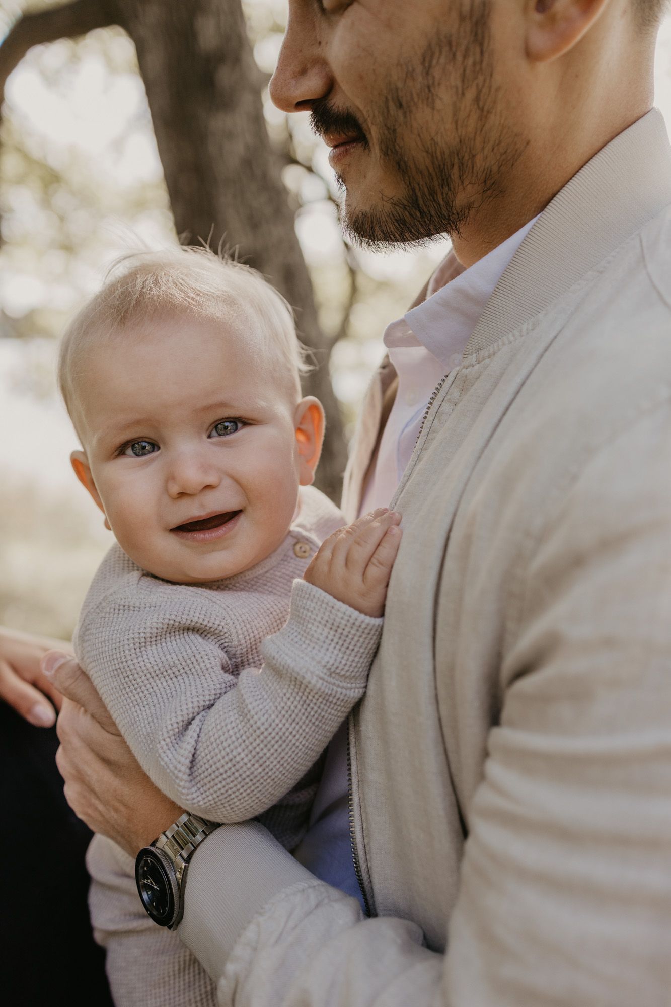 Close-up portrait of baby smiling while being held in warm outdoor lighting.