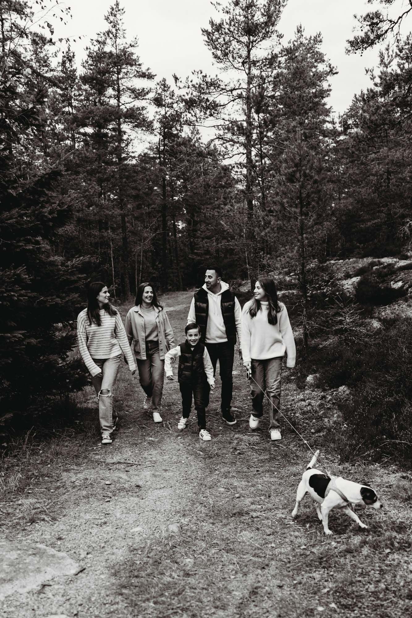 Black and white photo of a group walking on a forest path with a spotted dog.