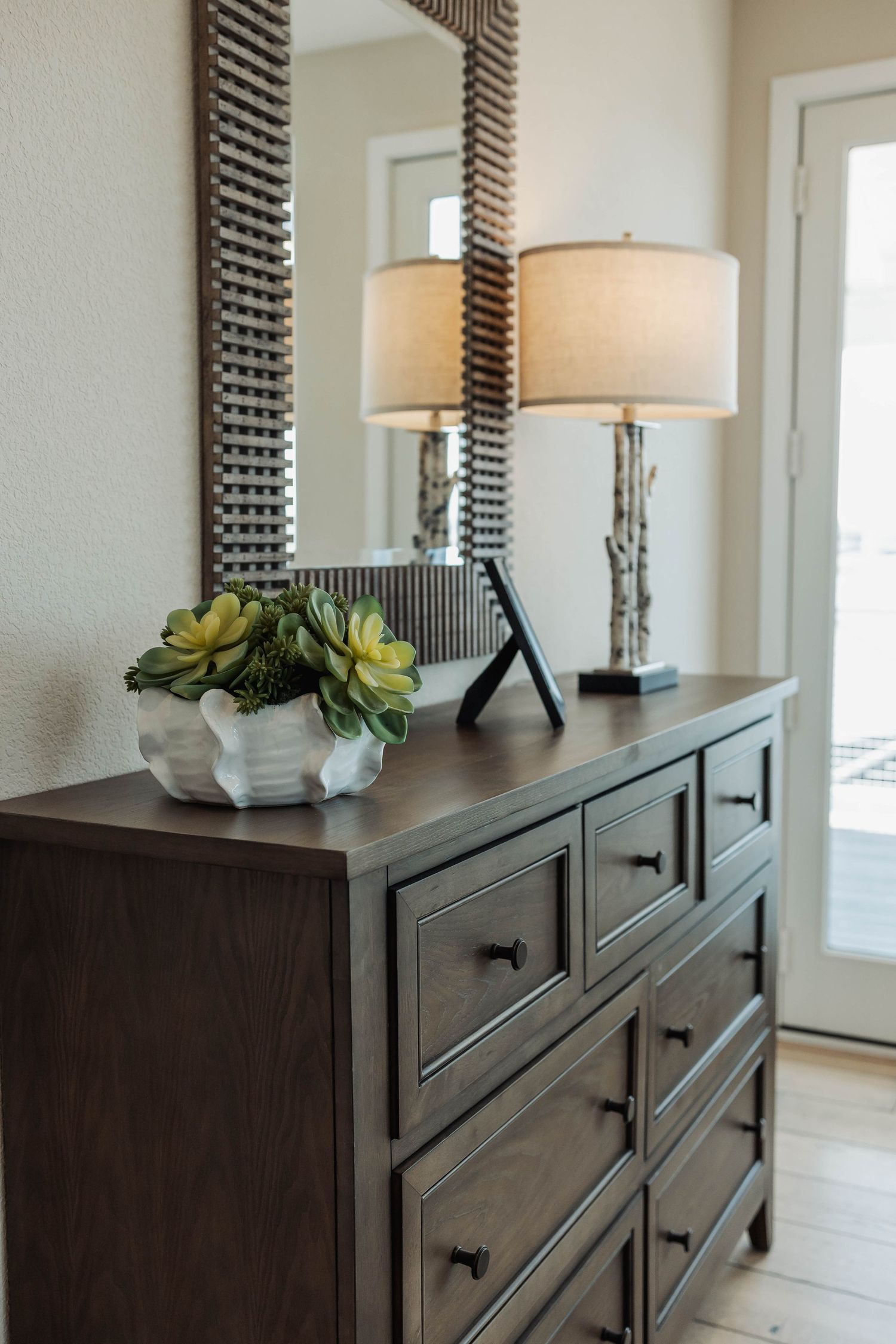 Dark wood dresser with modern table lamps and decorative mirrors creating an elegant bedroom focal point.