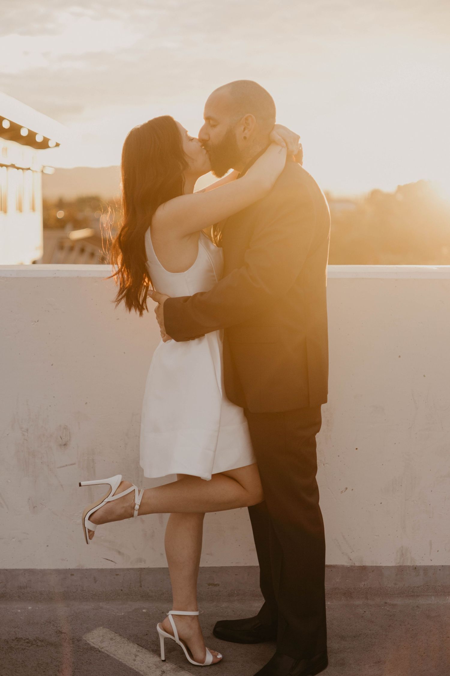 A romantic sunset silhouette of a couple embracing on a rooftop with warm golden light.