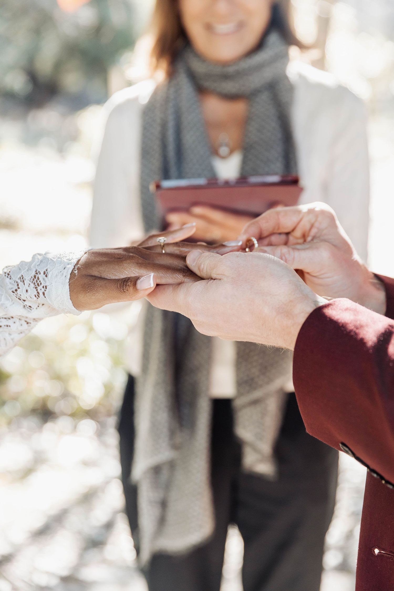 Close-up of hands during a ring exchange ceremony outdoors.