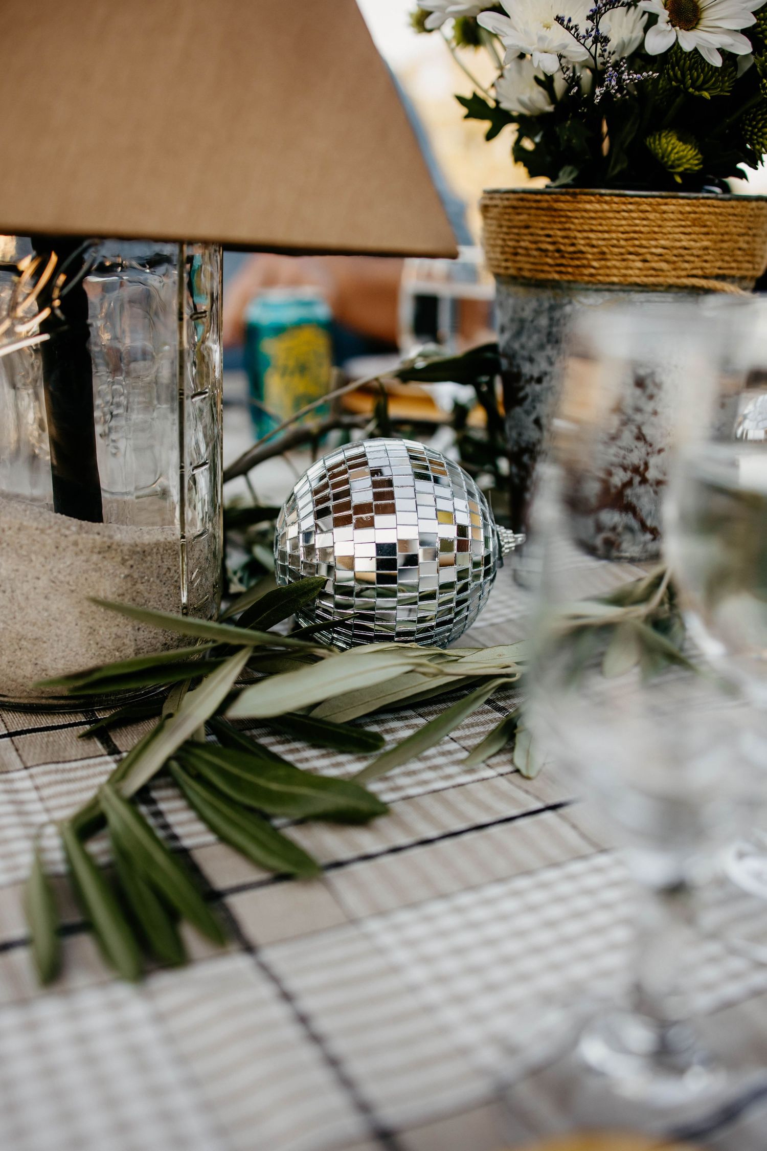 Table decorations featuring daisies, palm leaves, and disco balls on a checkered tablecloth.