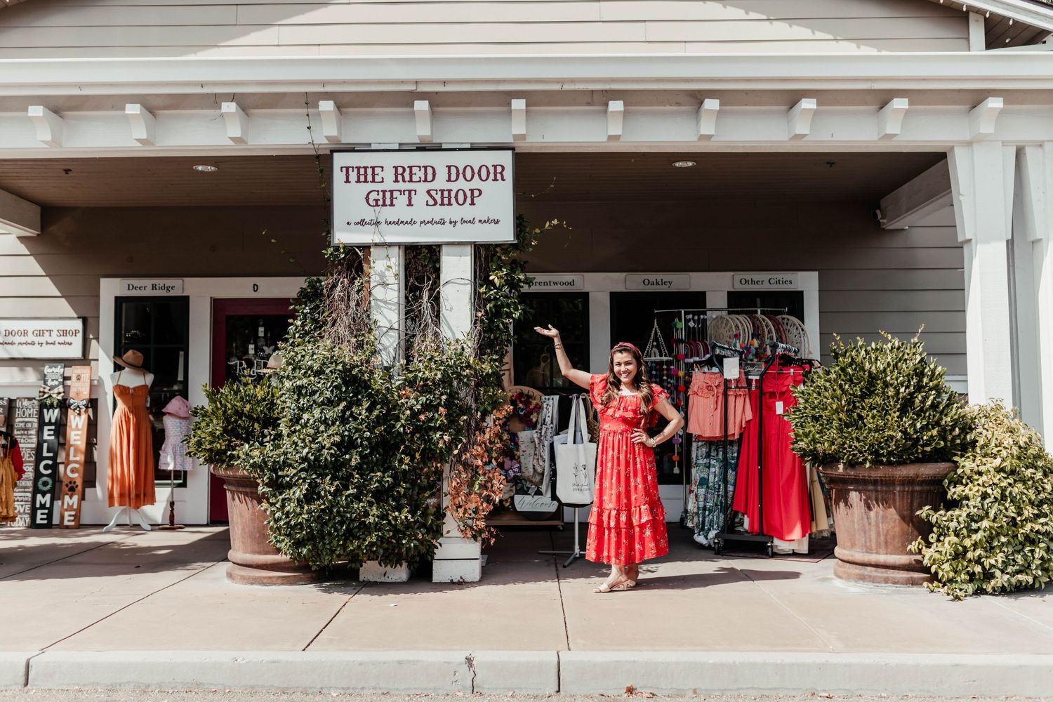 Exterior view of The Red Door gift shop with clothing racks and potted plants outside.