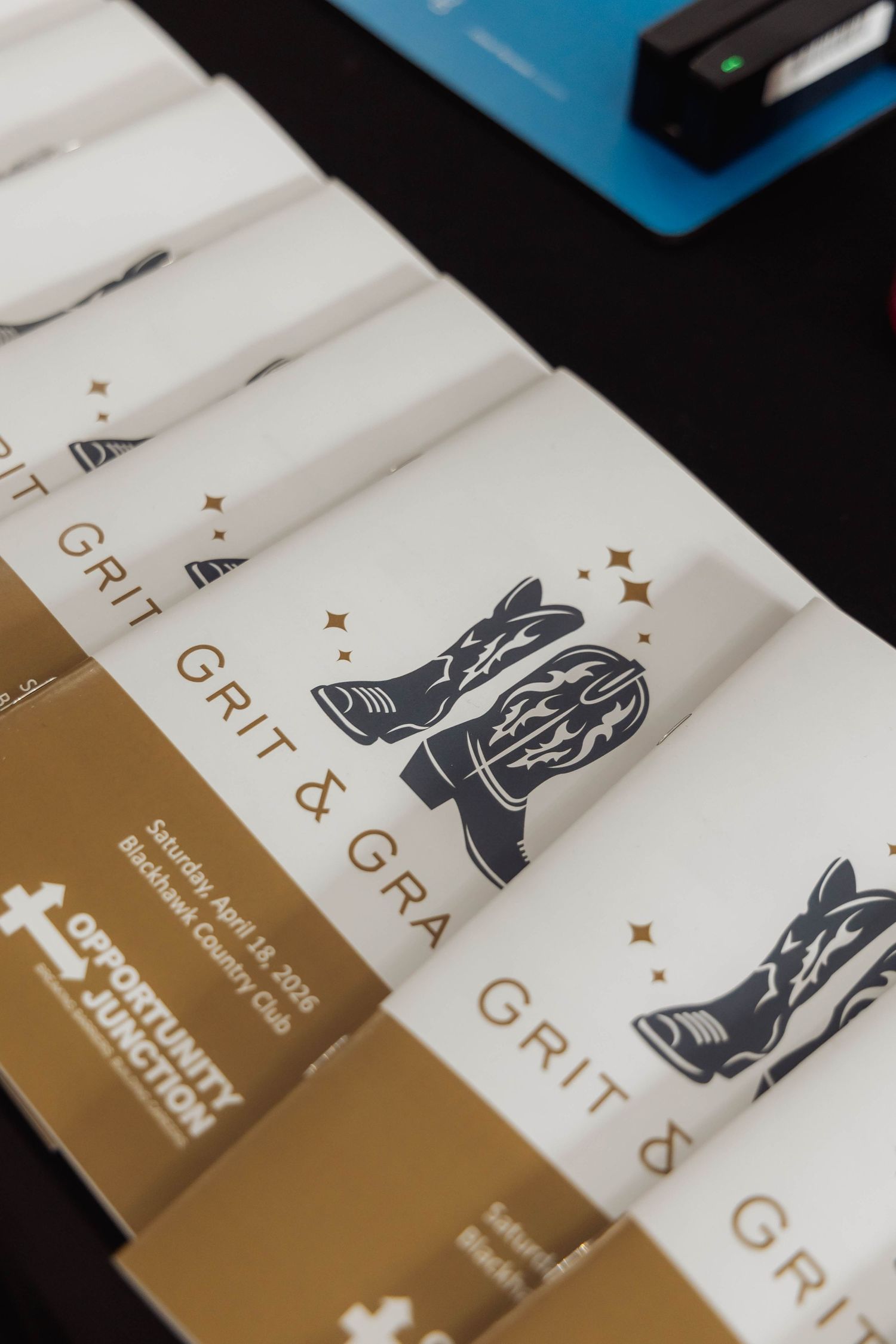White programs for Grit & Grace event at Blackhawk Country Club featuring cowboy boot logo and Opportunity Junction branding.
