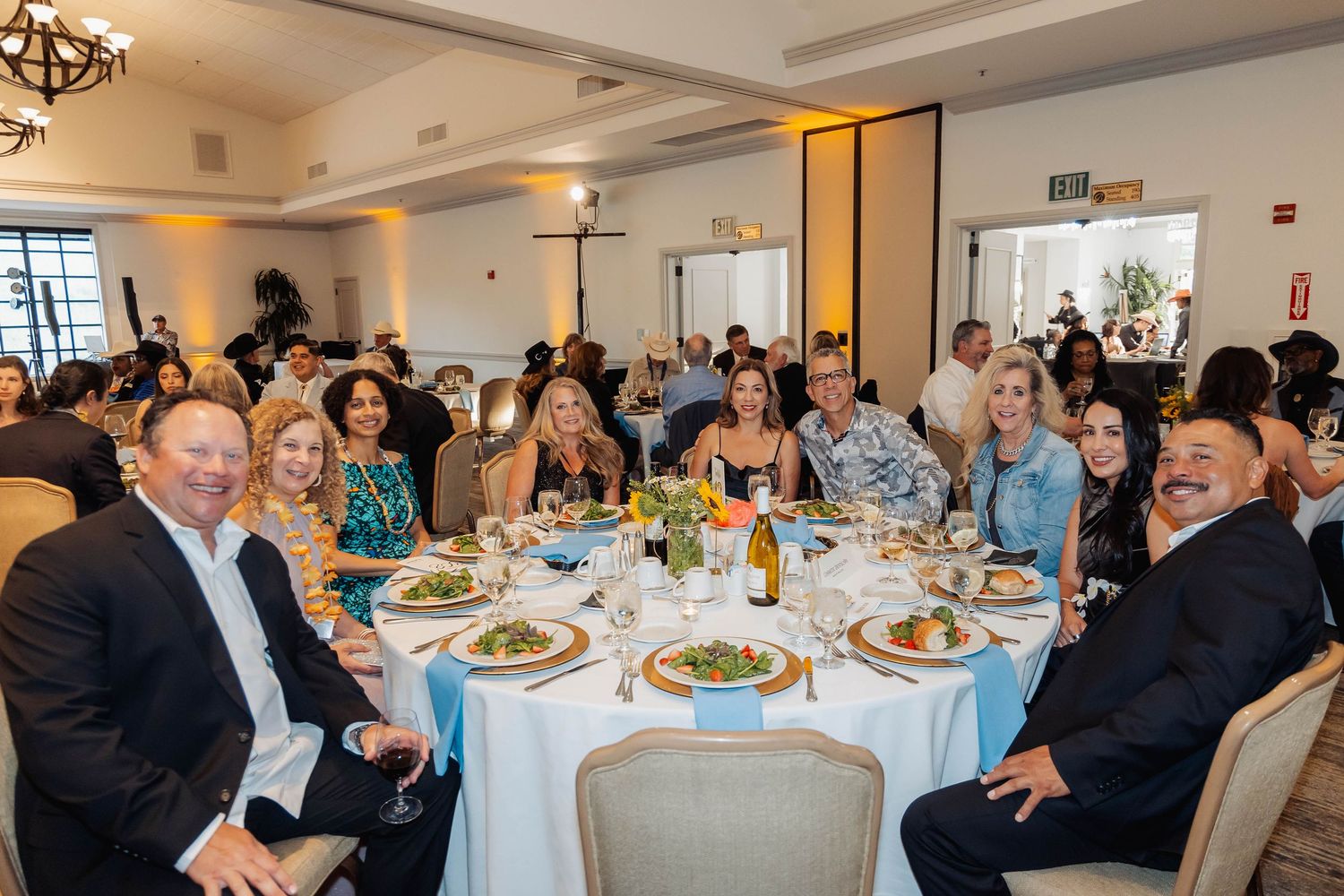 Guests smiling and posing at a round banquet table during a formal dinner event in an elegant white venue.