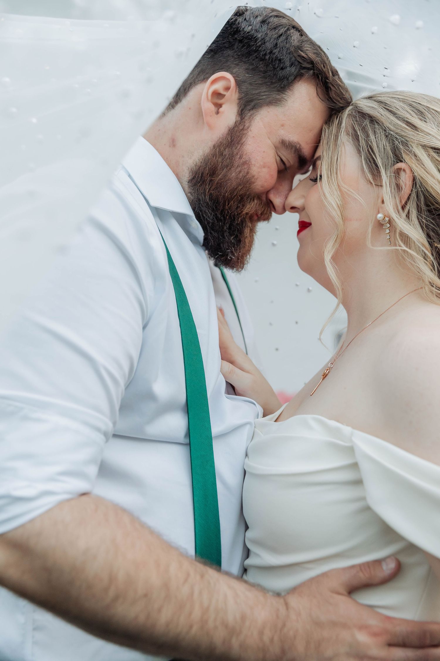Intimate wedding couple moment with green tie detail and white attire.