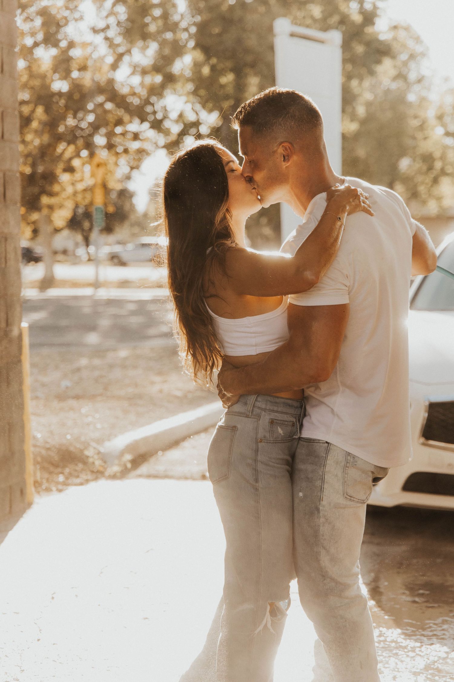 Romantic couple embracing in golden hour light against outdoor backdrop.