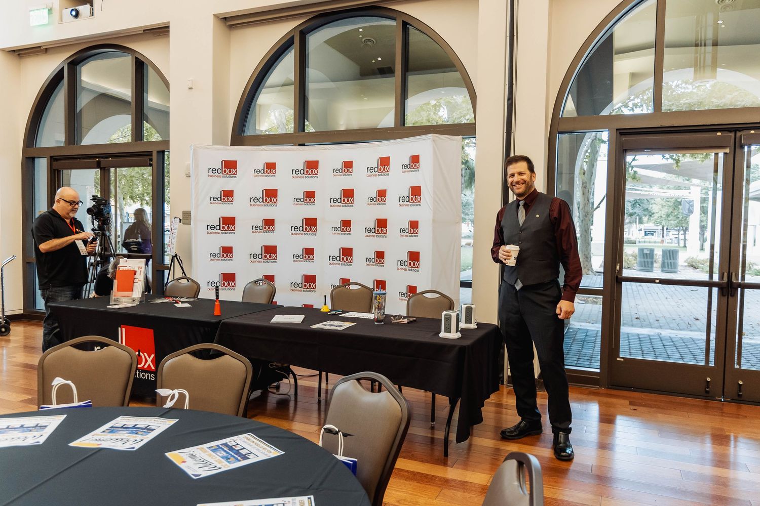 Event setup with backdrop and registration table in elegant venue with arched windows.