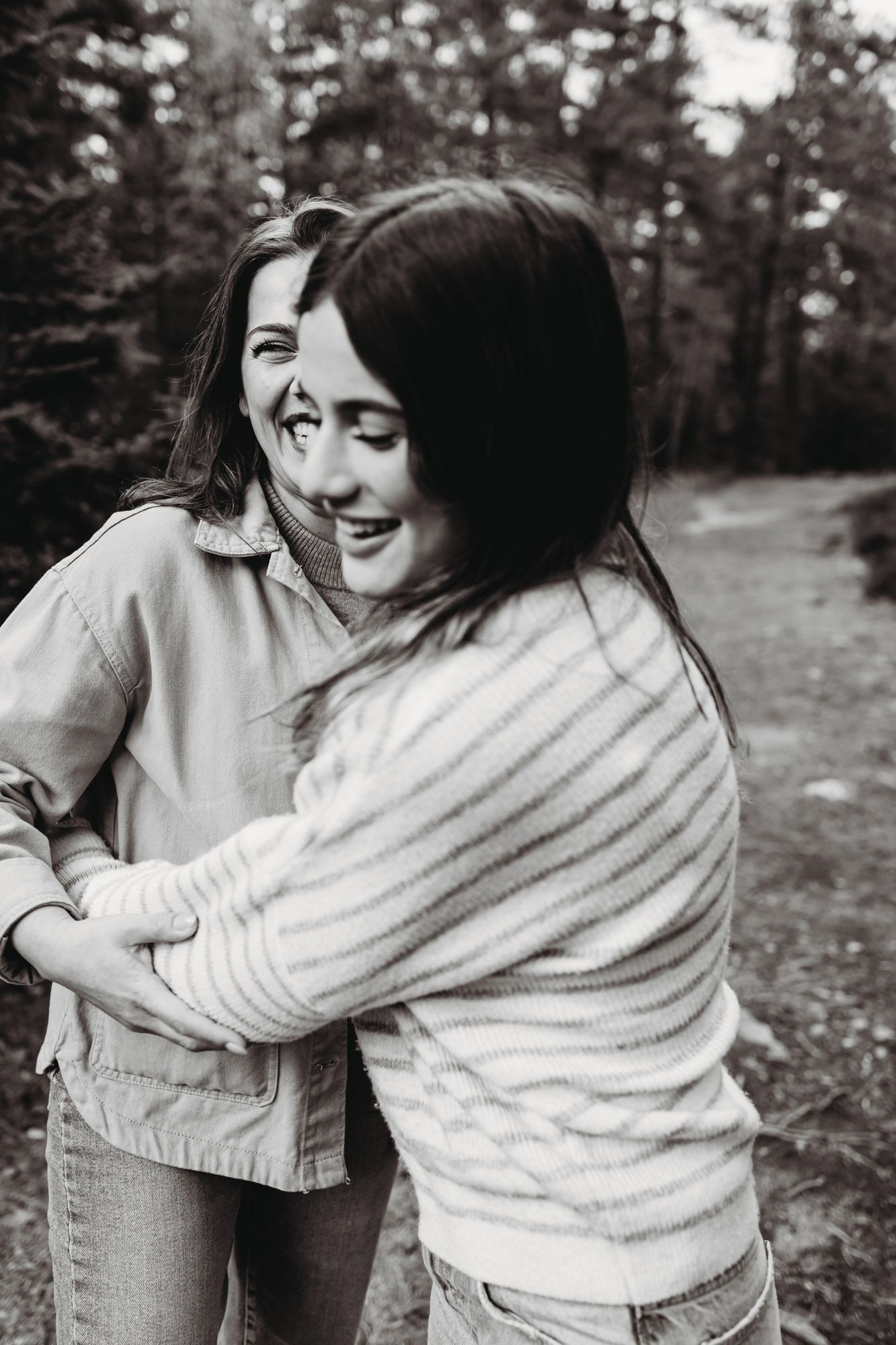 Black and white photo of two people embracing and laughing together on a wooded trail.