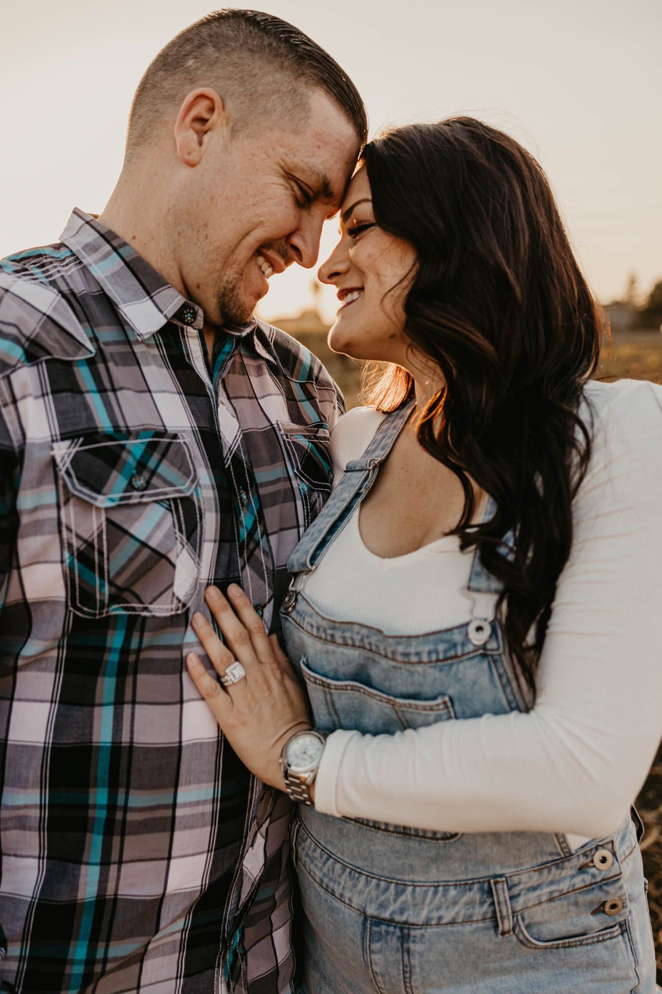 A couple in casual clothing embraces while sharing an intimate moment during sunset.