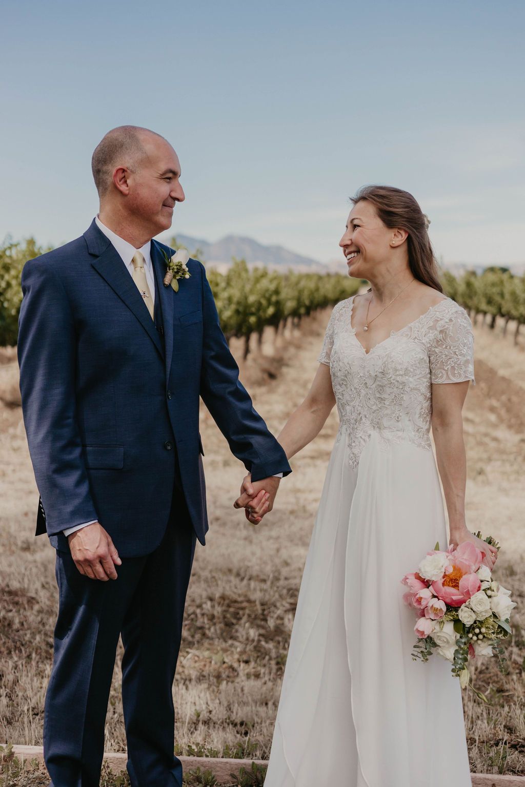 Newlyweds share a joyful moment together in a vineyard while holding hands on their wedding day.
