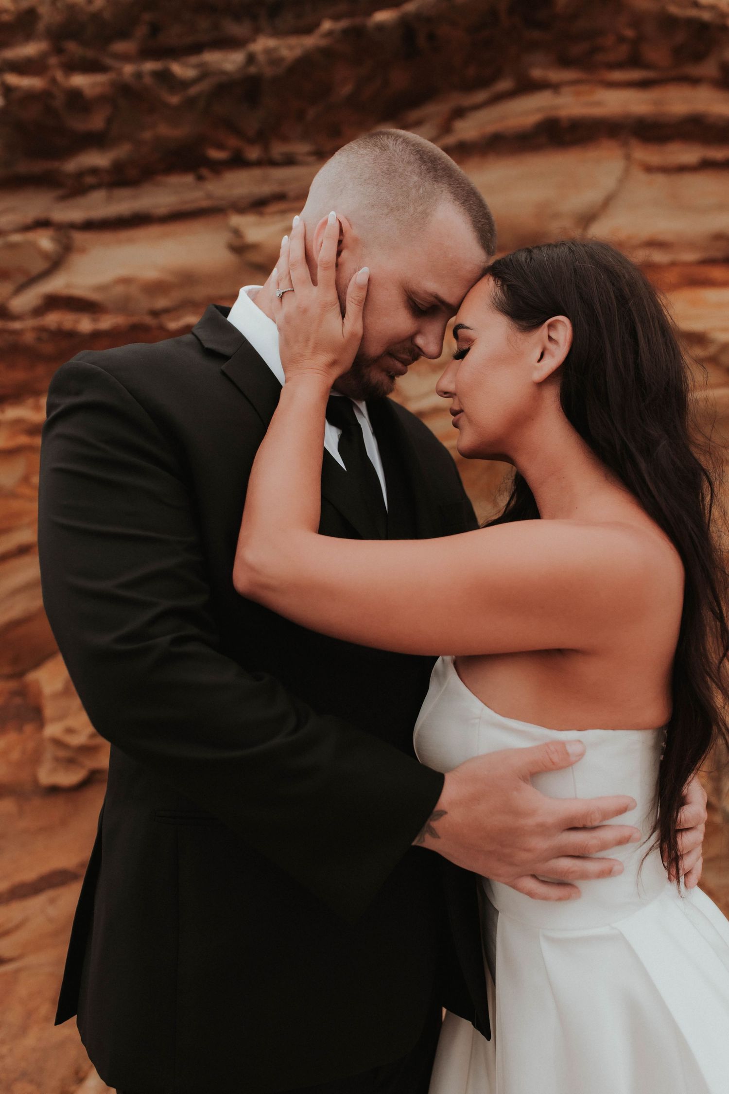 Intimate wedding portrait of a couple embracing against red rock formations at sunset.