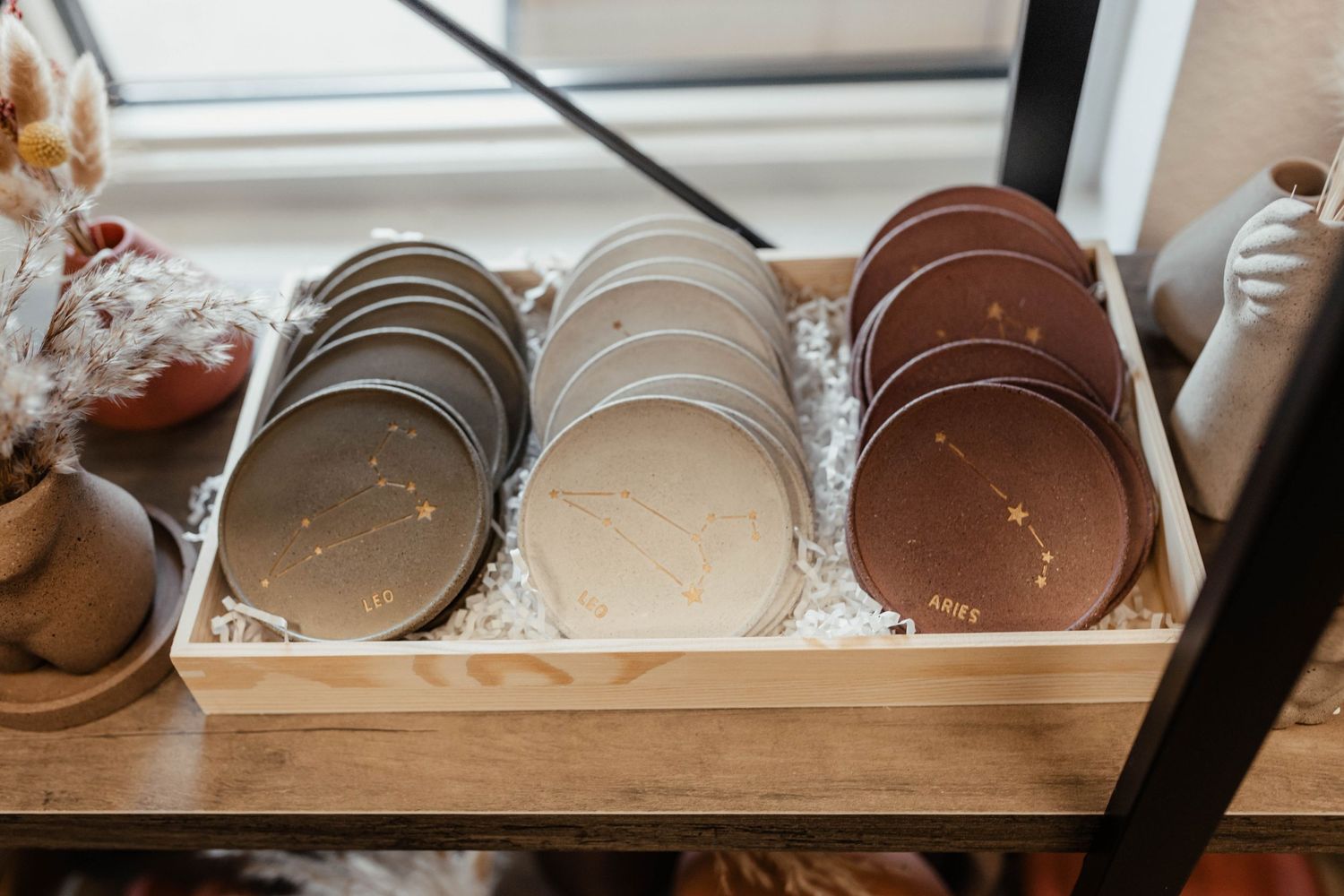 Display of circular ceramic plates in various neutral tones arranged in wooden box.