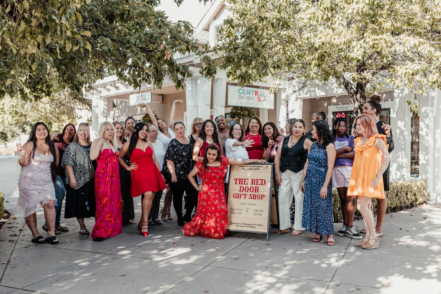 A large group gathered outdoors wearing red and blue dresses and casual attire at a storefront.