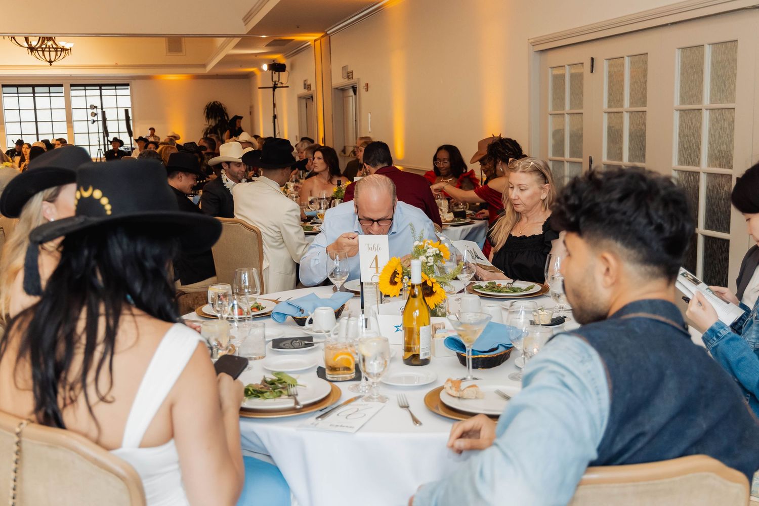 Diverse guests enjoy a formal banquet dinner at decorated round tables in a warmly lit elegant venue.
