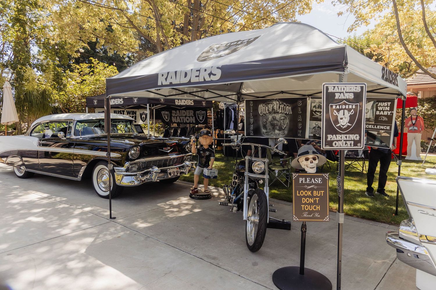 Raiders NFL fan tailgate setup with classic black vintage car, tent, and memorabilia display outdoors.