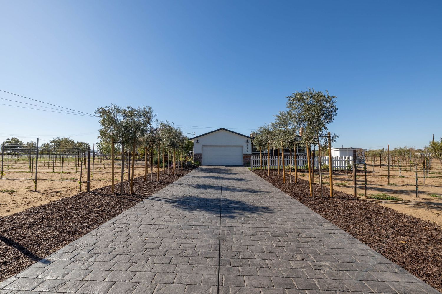 Long paved driveway leading to property under clear blue sky.