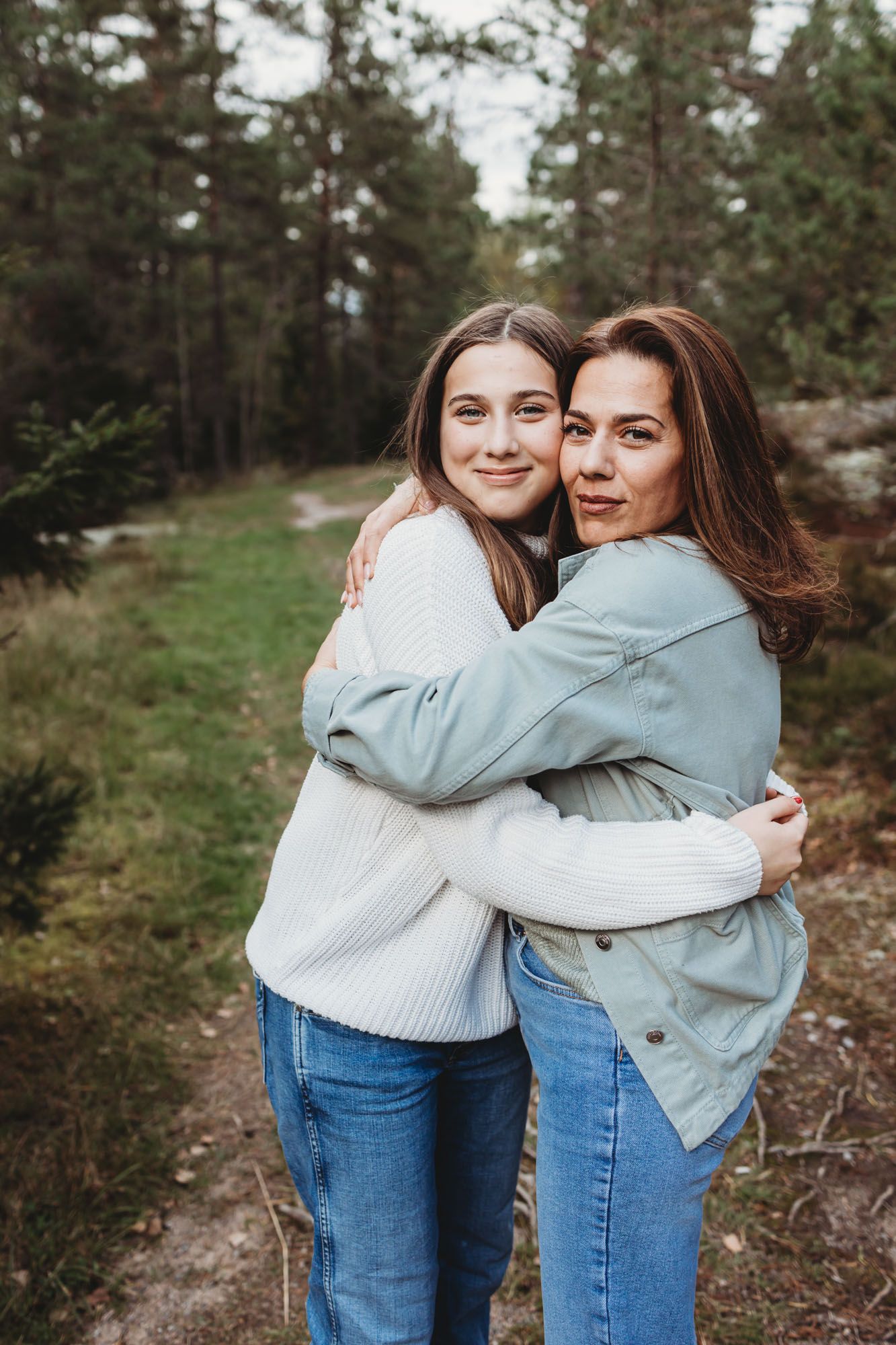 Two people in cozy sweaters embrace while standing on a forest trail.