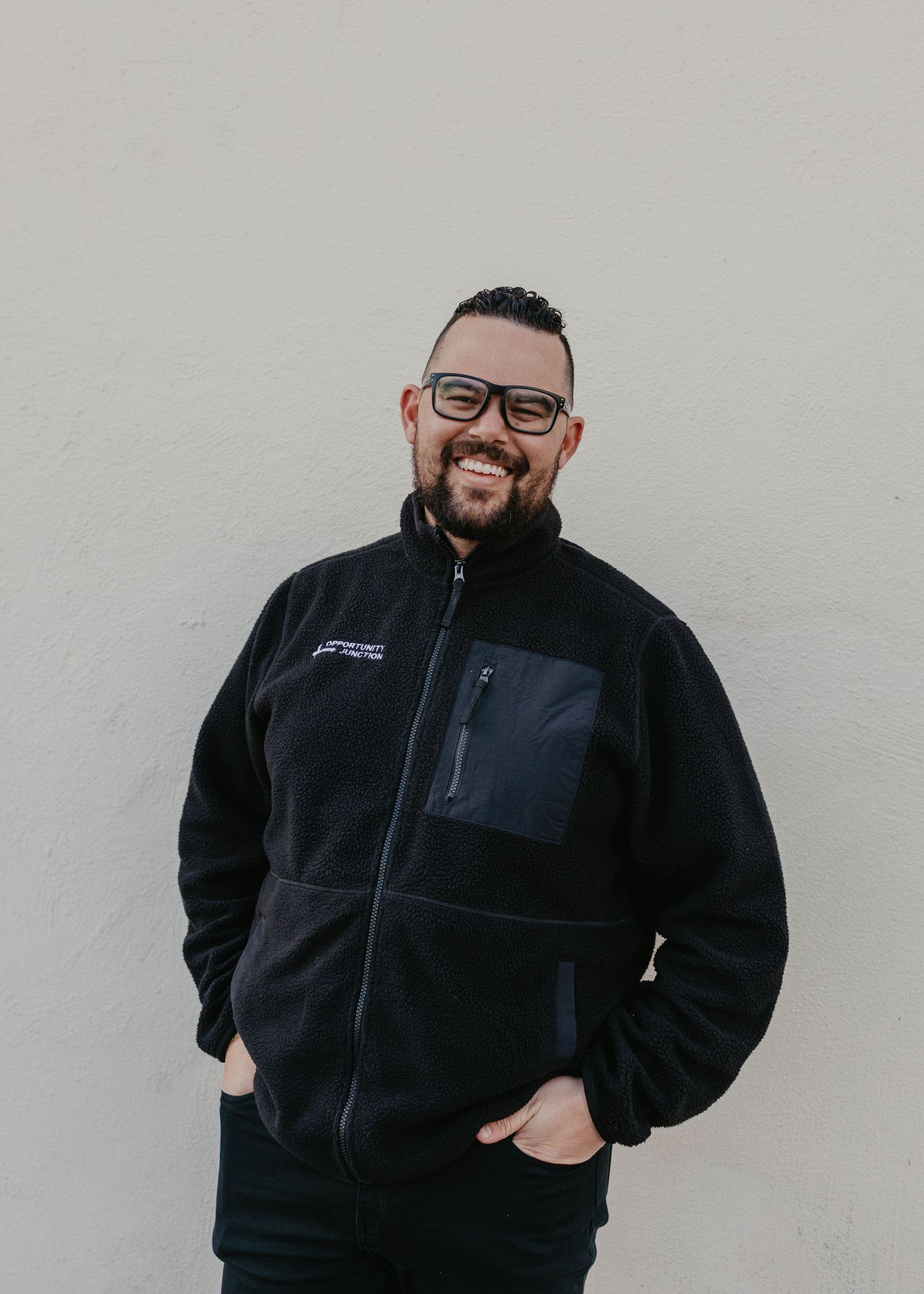 Staff member in black fleece jacket posing against light colored wall.