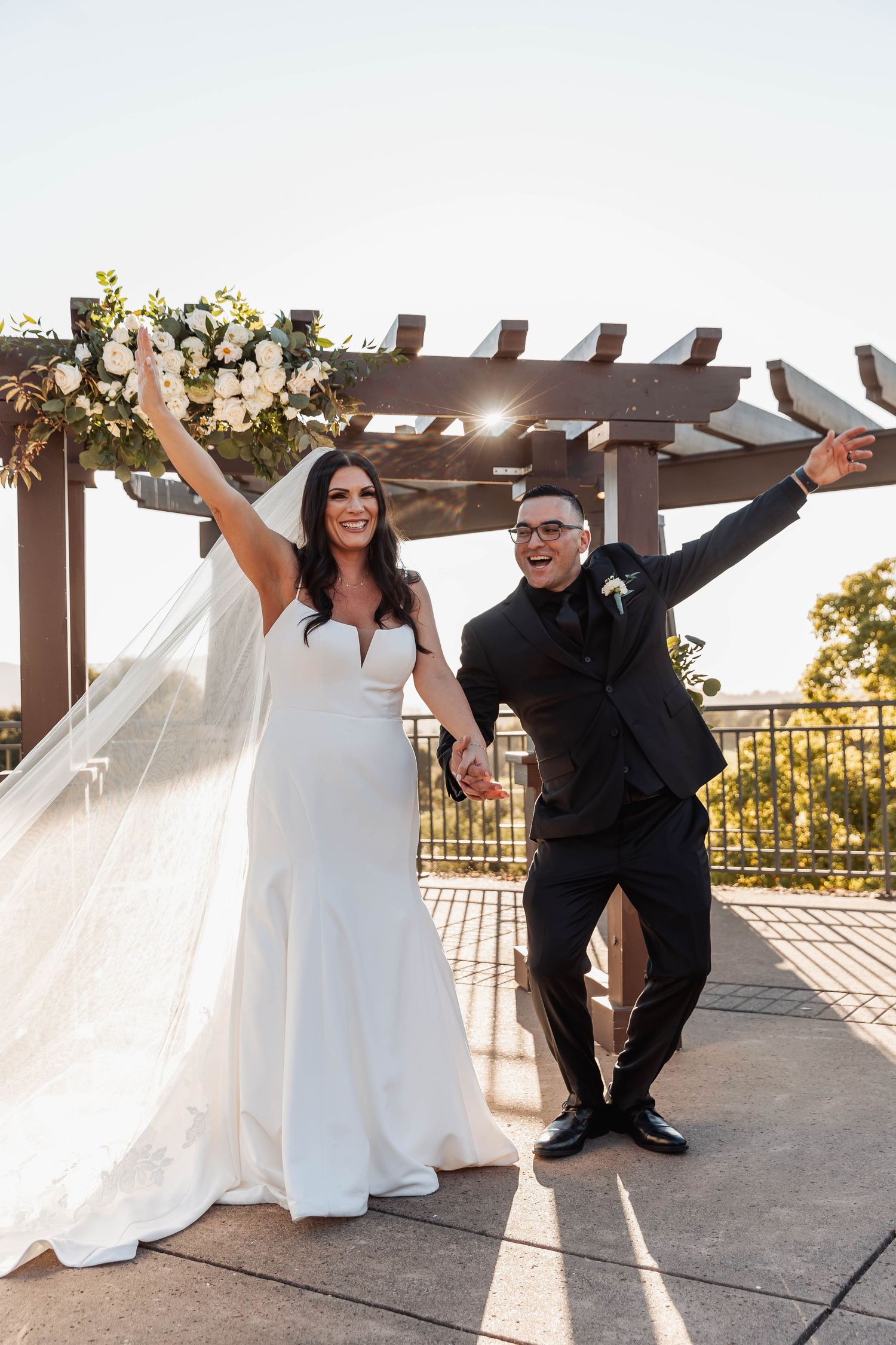 Newlyweds striking fun poses under outdoor pergola at sunset.