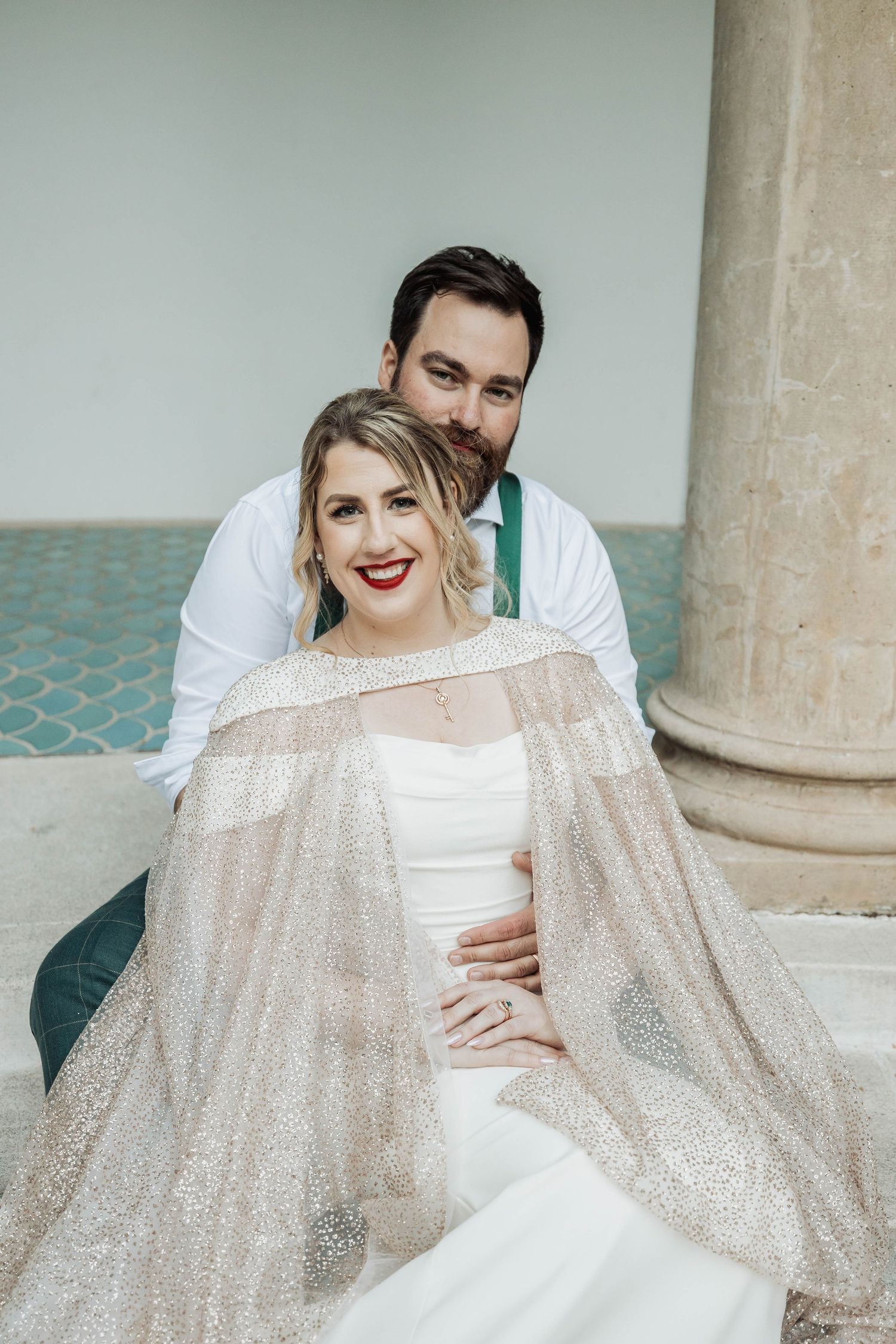 Wedding couple posing by classical columns with sparkly sheer fabric.