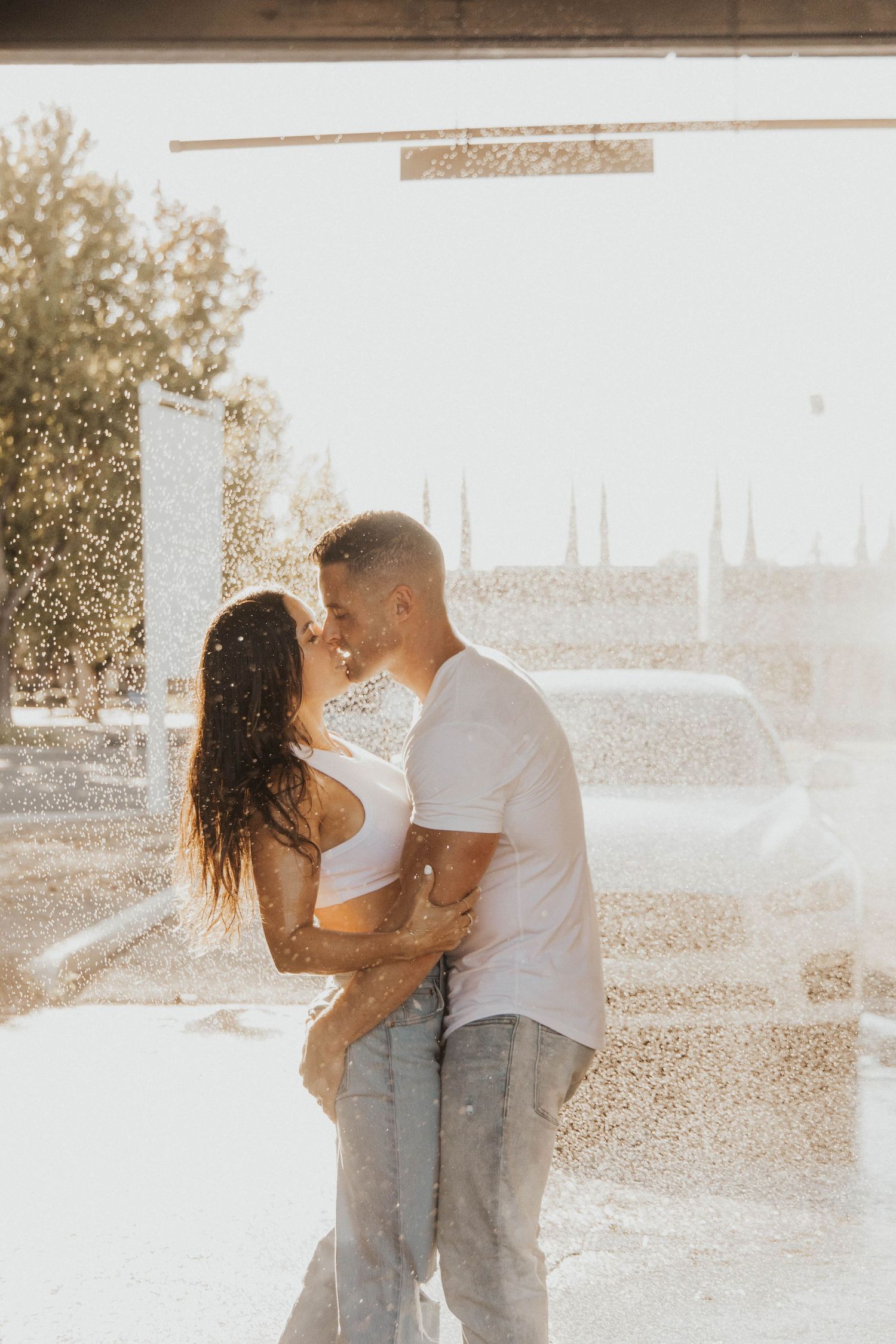 Romantic couple embracing in sunlit setting wearing casual white tops and jeans.